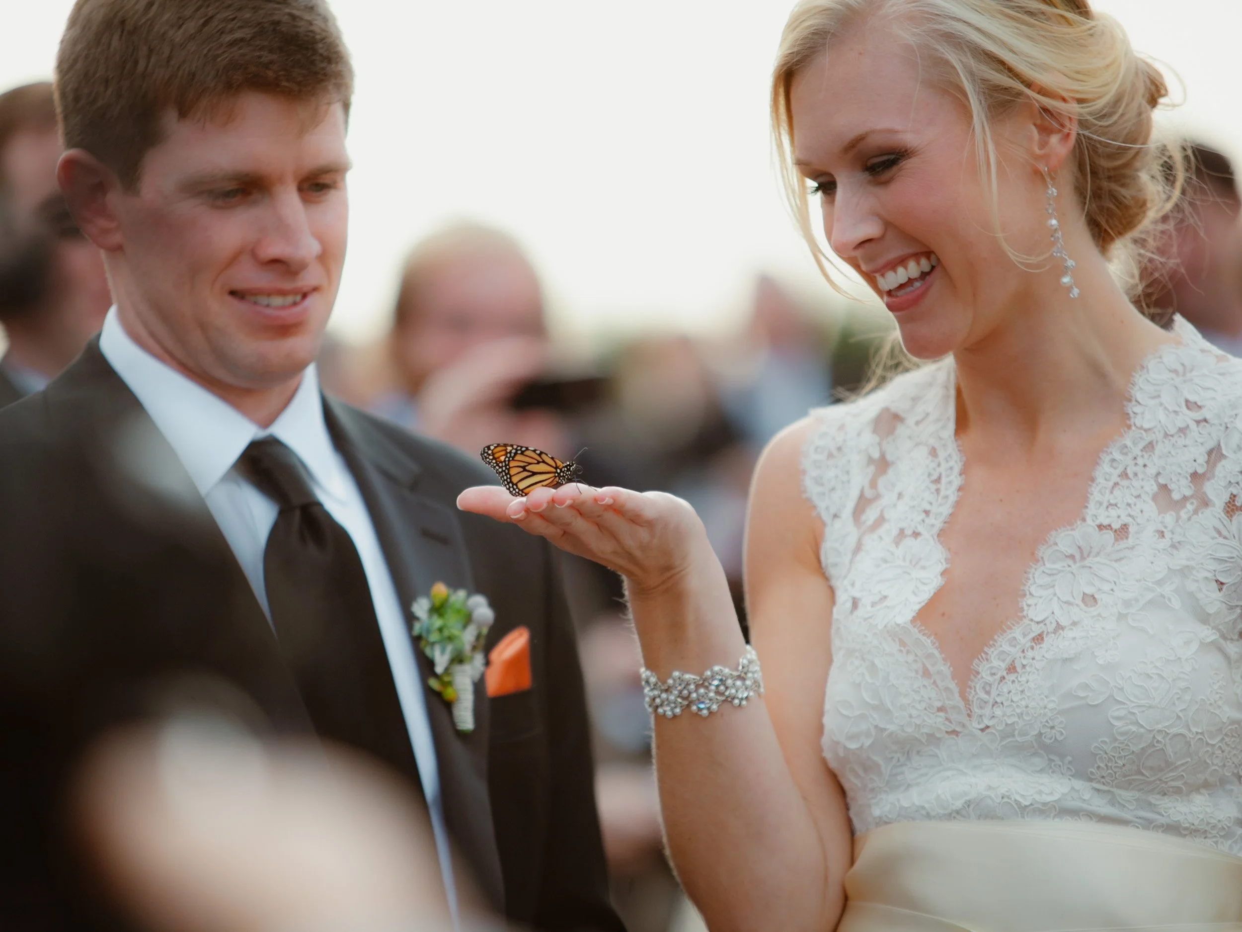 A bride and groom at a wedding ceremony, with the bride holding a butterfly on her hand.