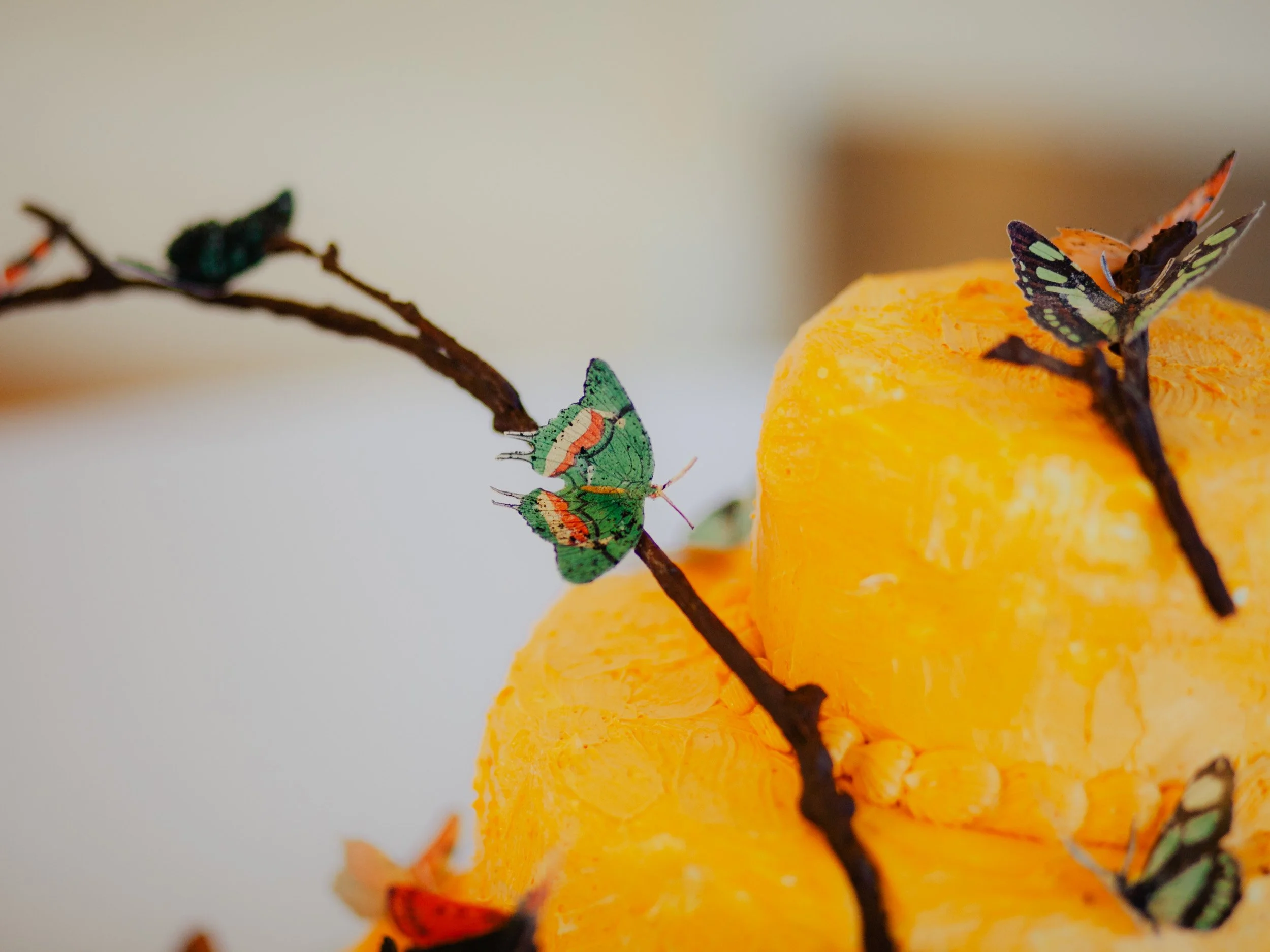 Decorative scene with edible butterflies on a yellow wedding cake against a neutral background.