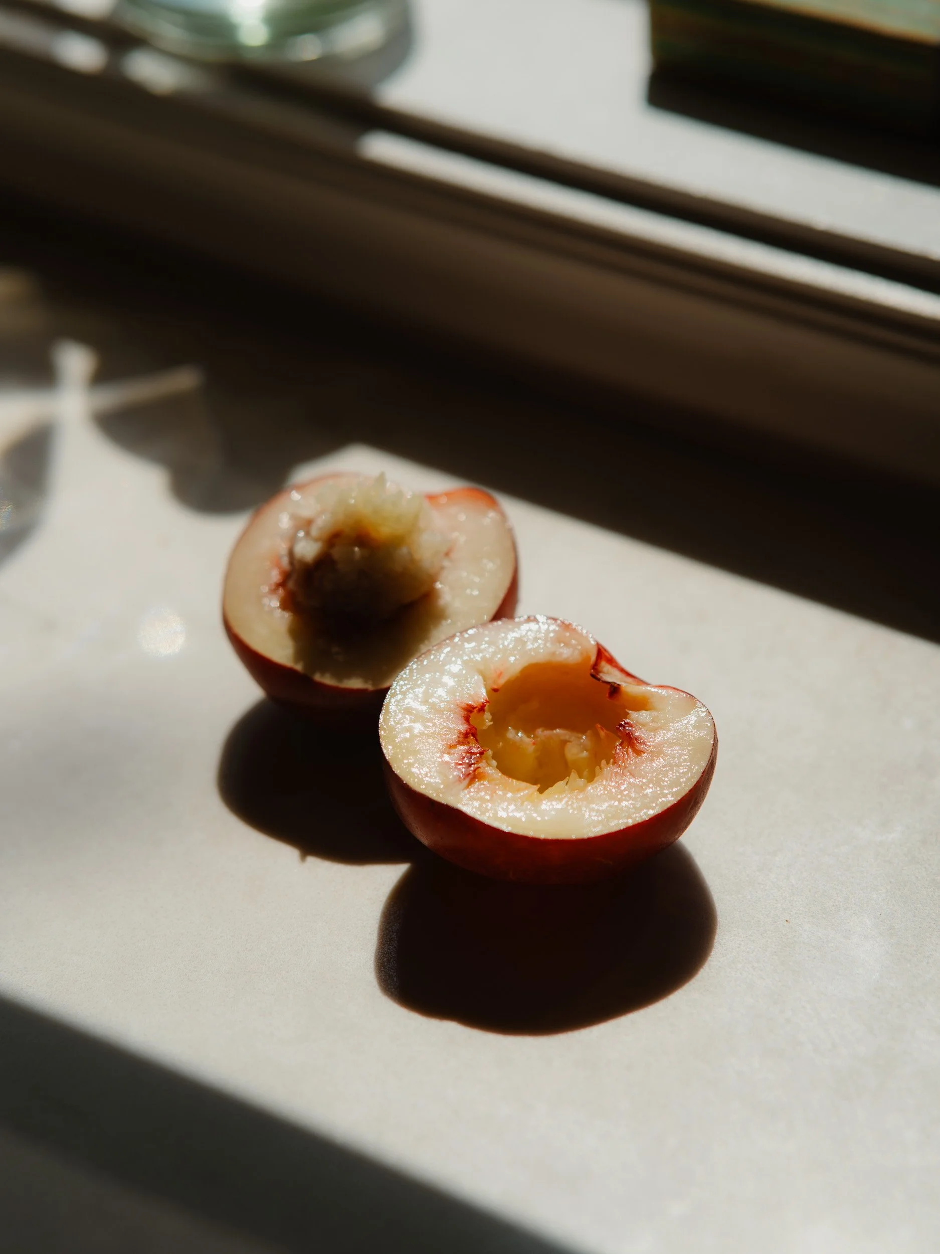 Half of a red and white cherry with exposed pit, sitting on a white surface near a windowsill with natural sunlight.