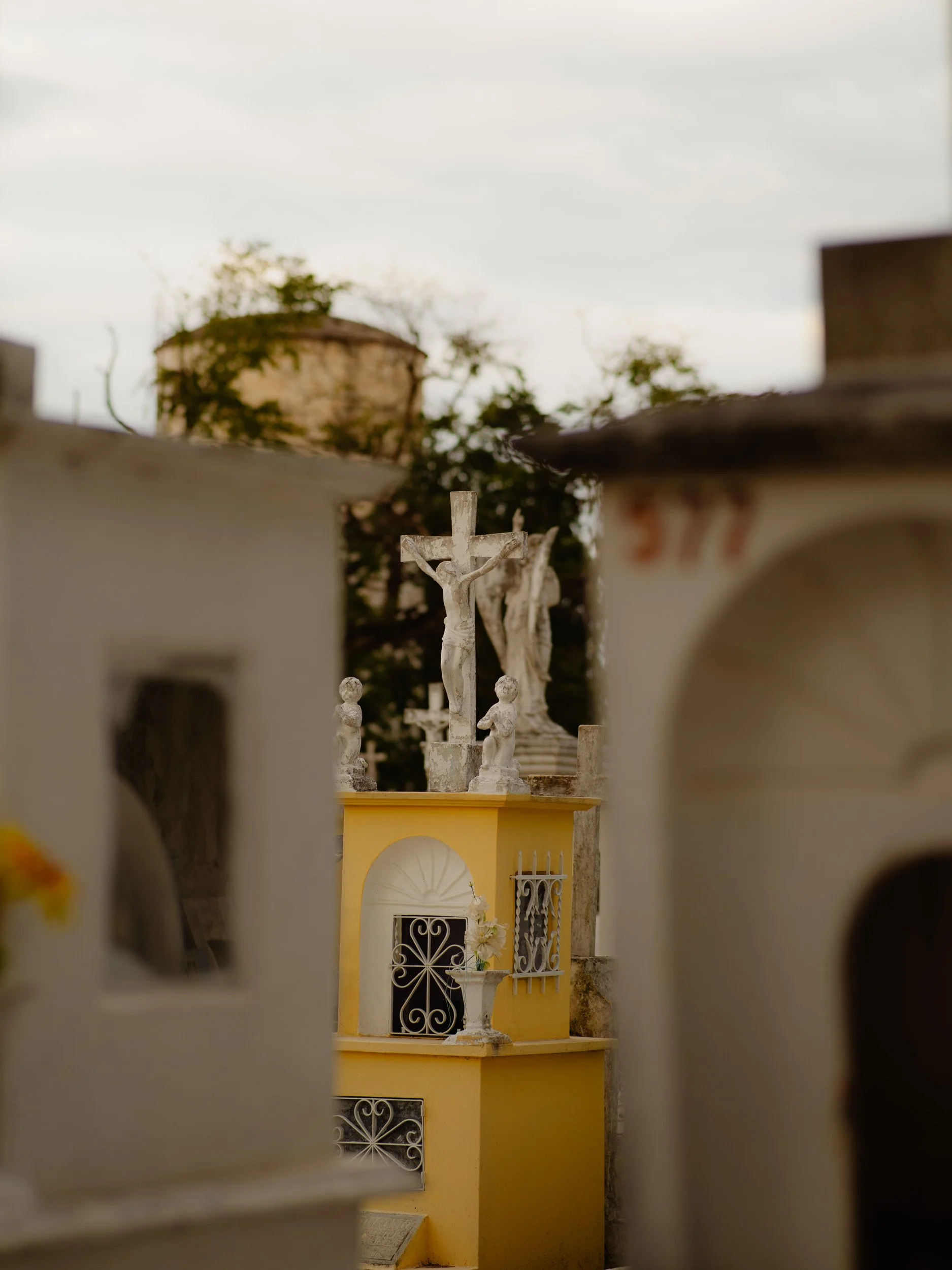 Graveyard with statues of Jesus on the crucifix, framed by tombs and mausoleums, with a cloudy sky in the background.