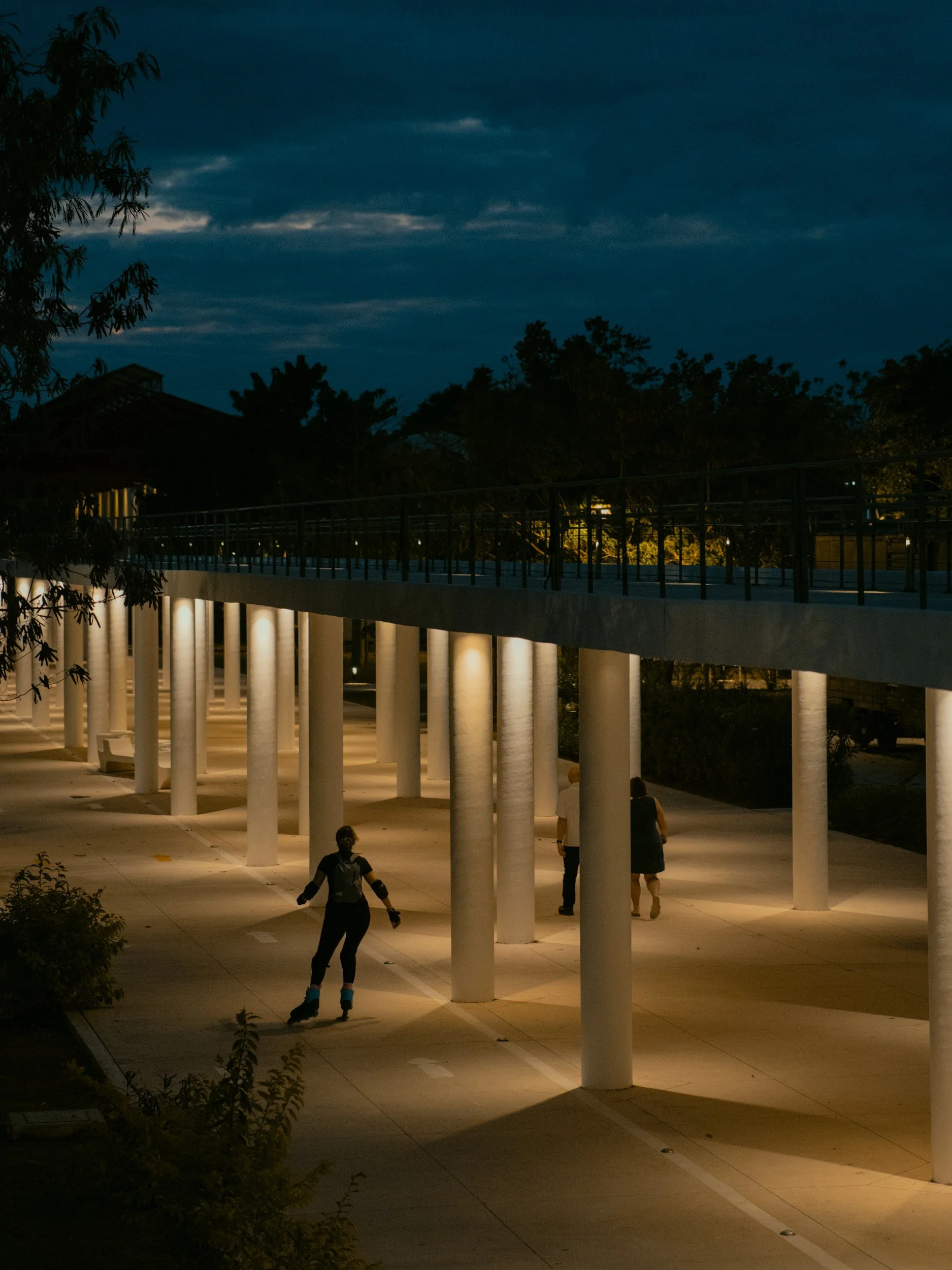People roller skating under a lit walkway with tall columns at dusk.