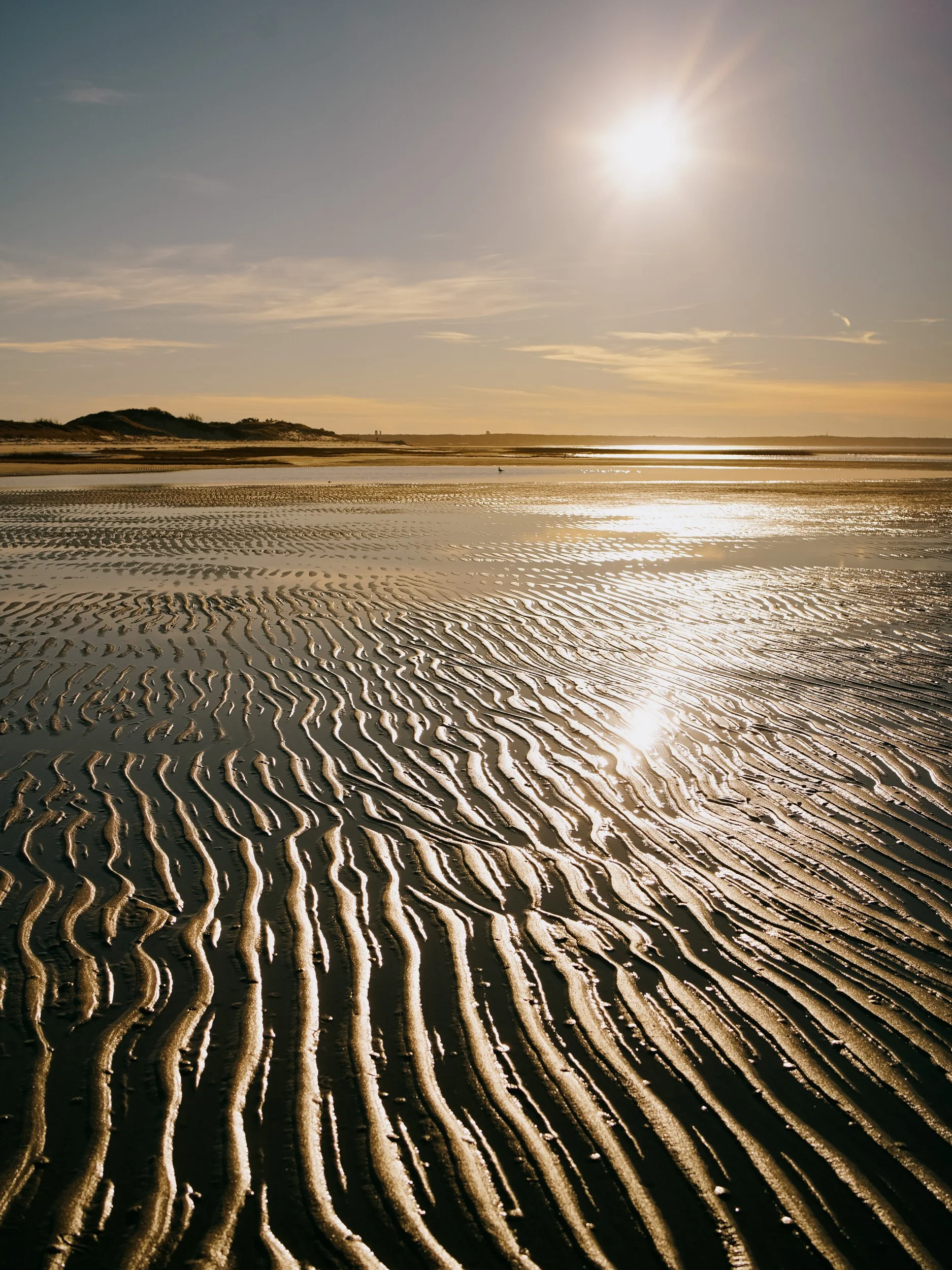Sun shining brightly over a beach with rippled sand patterns and a calm reflective surface