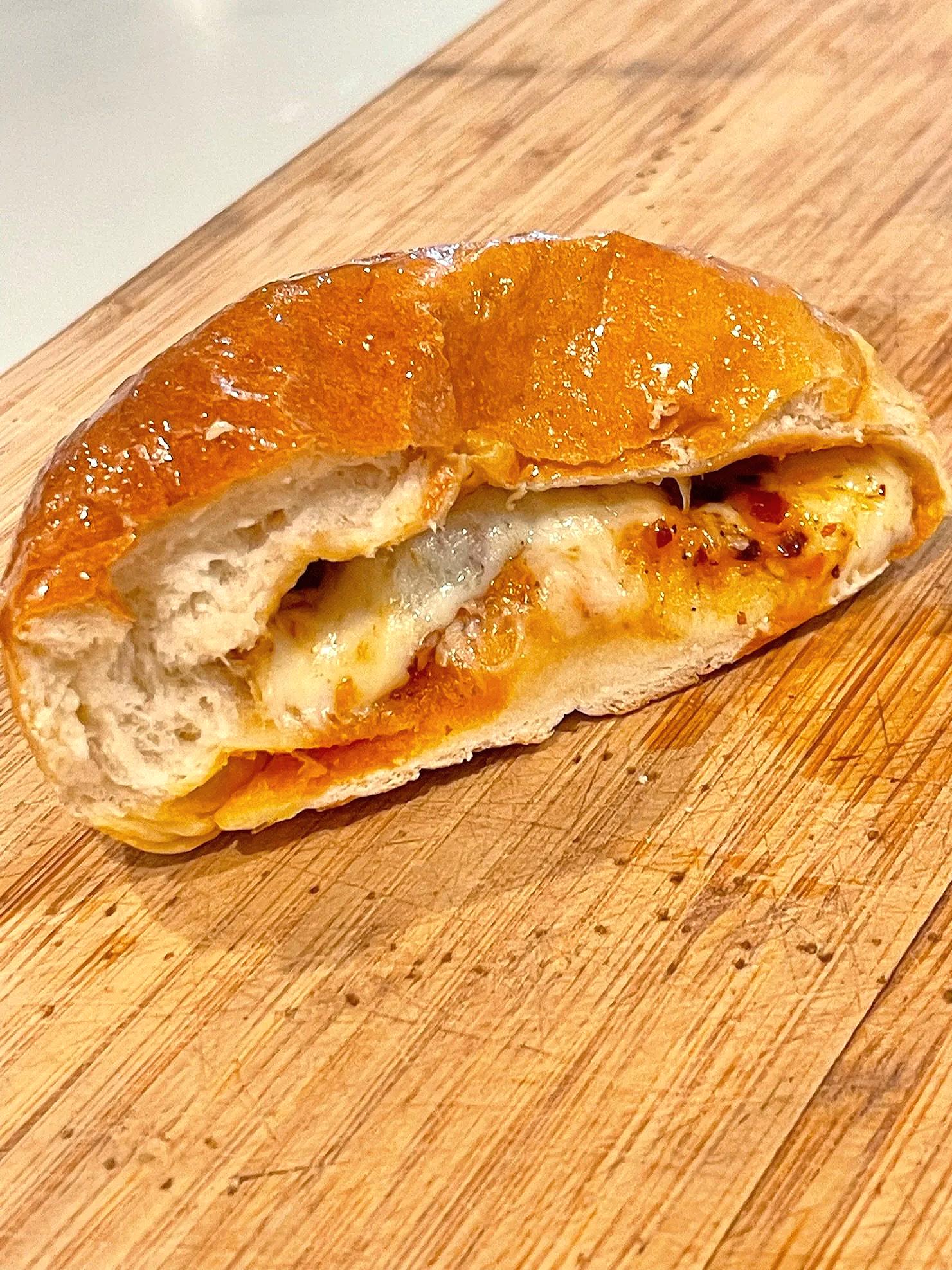 A partially eaten cheese and pepperoni stuffed bread roll on a wooden cutting board.