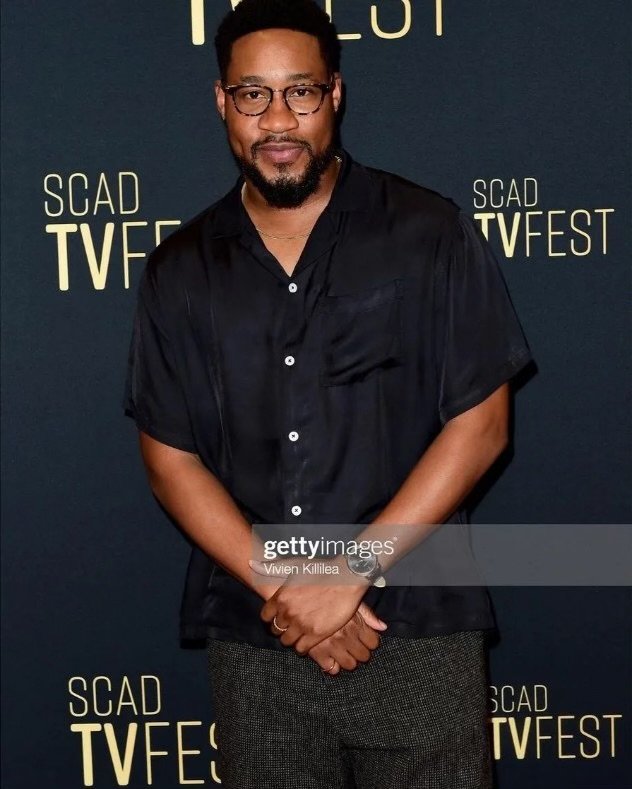A man with glasses and a beard wearing a black button-up shirt, standing in front of a dark backdrop with yellow text that reads "SCAD TV FEST".