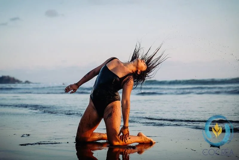 Une femme qui pose dans l'eau de la mer, en arrière-plan un ciel nuageux.