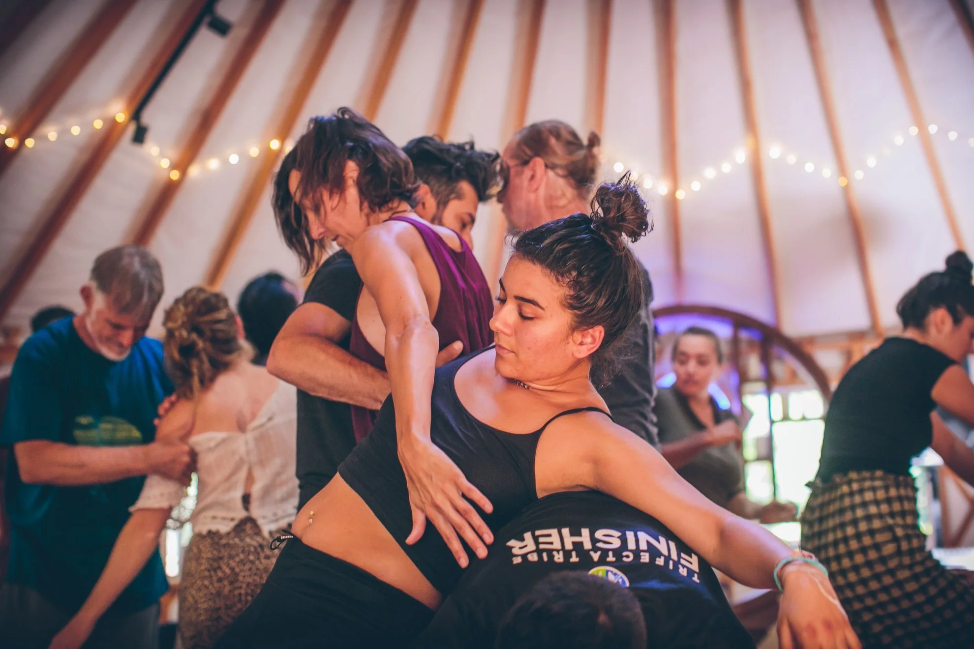 Groupe de personnes dansant lors d'une fête dans une cabane en bois, décorée de guirlandes lumineuses.