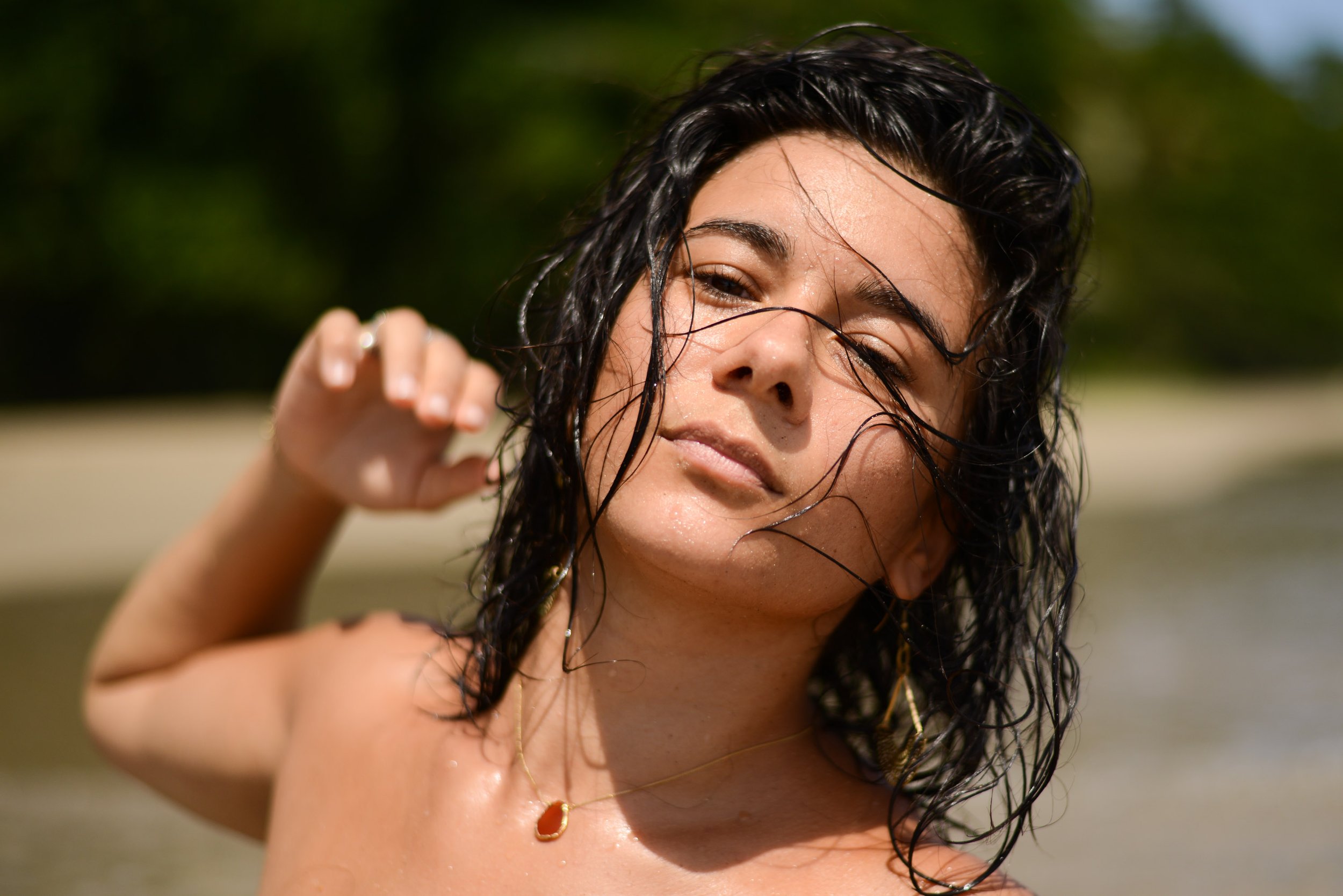 Femme avec cheveux mouillés, souriant légèrement, en extérieur sous le soleil.