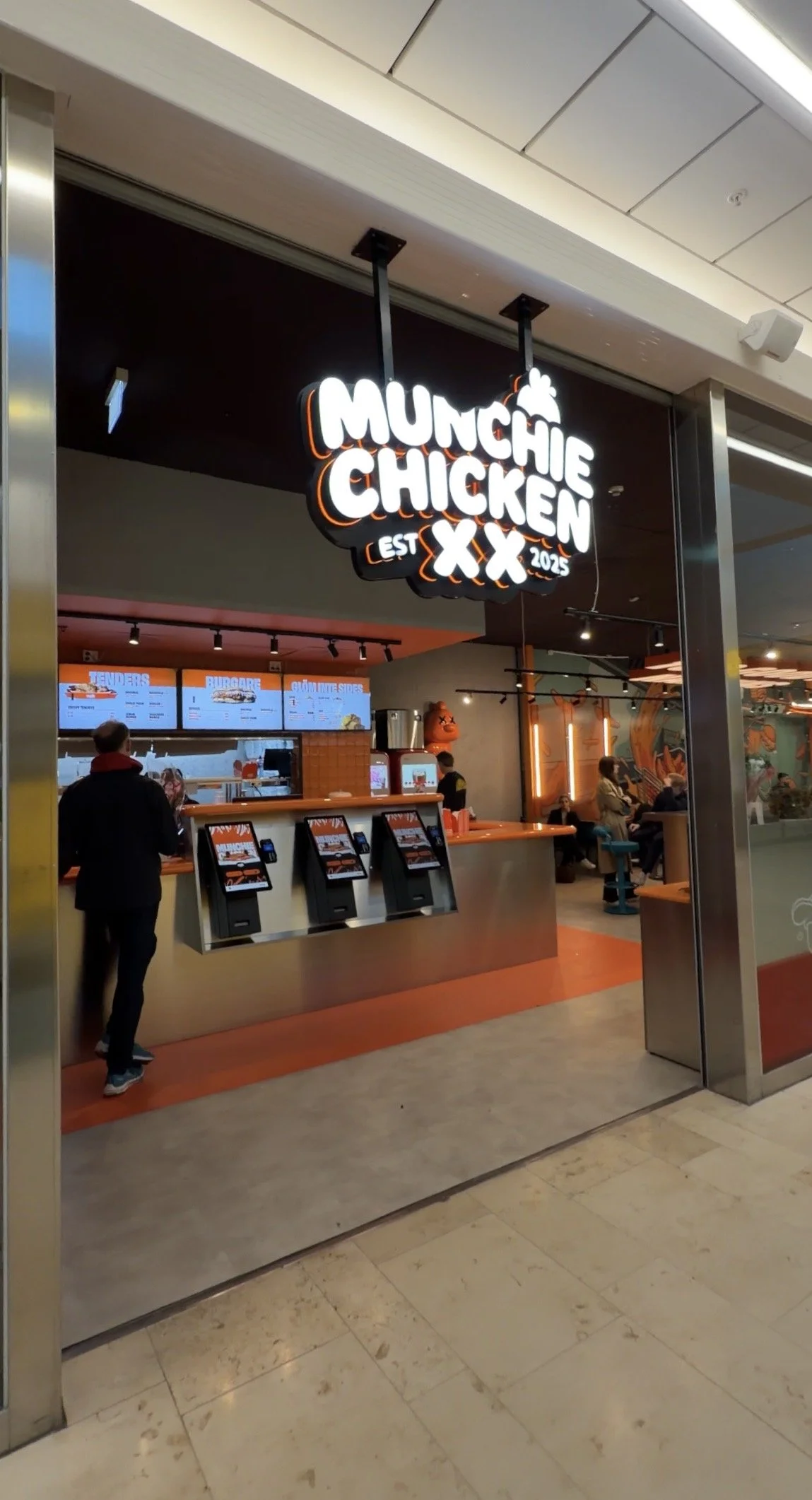 Munchie Chicken-restaurang i Täby Centrum med modern inredning, digitala beställningskiosker och en tydlig upplyst skylt vid entrén. Här serveras krispig kyckling, burgare och sides i en avslappnad miljö mitt i köpcentrumet.