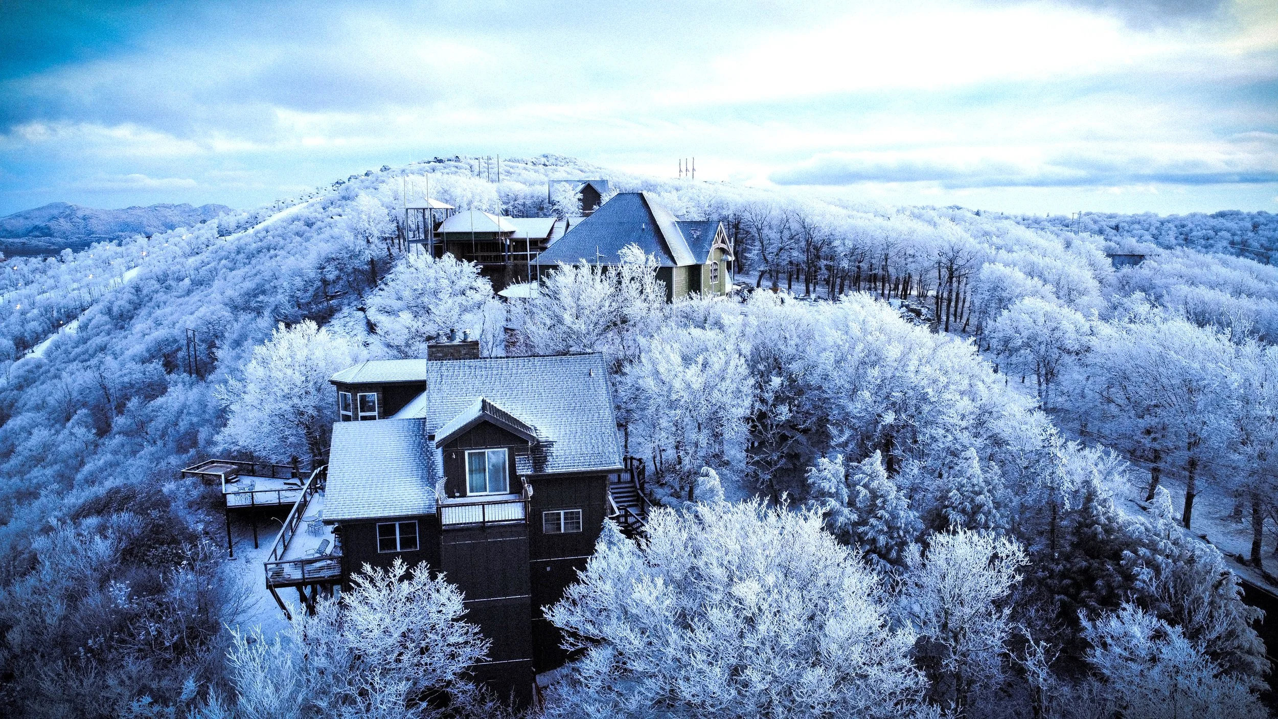 Snow-covered houses on a hillside surrounded by frost-covered trees under a cloudy sky.
