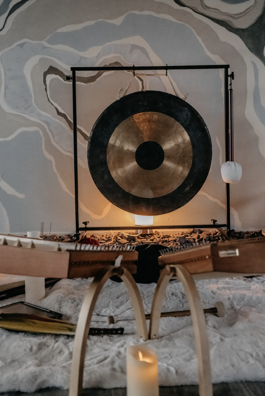 A large gong with a bronze center and black outer ring, mounted on a black metal frame, illuminated by soft lighting, with a wall mural in the background.