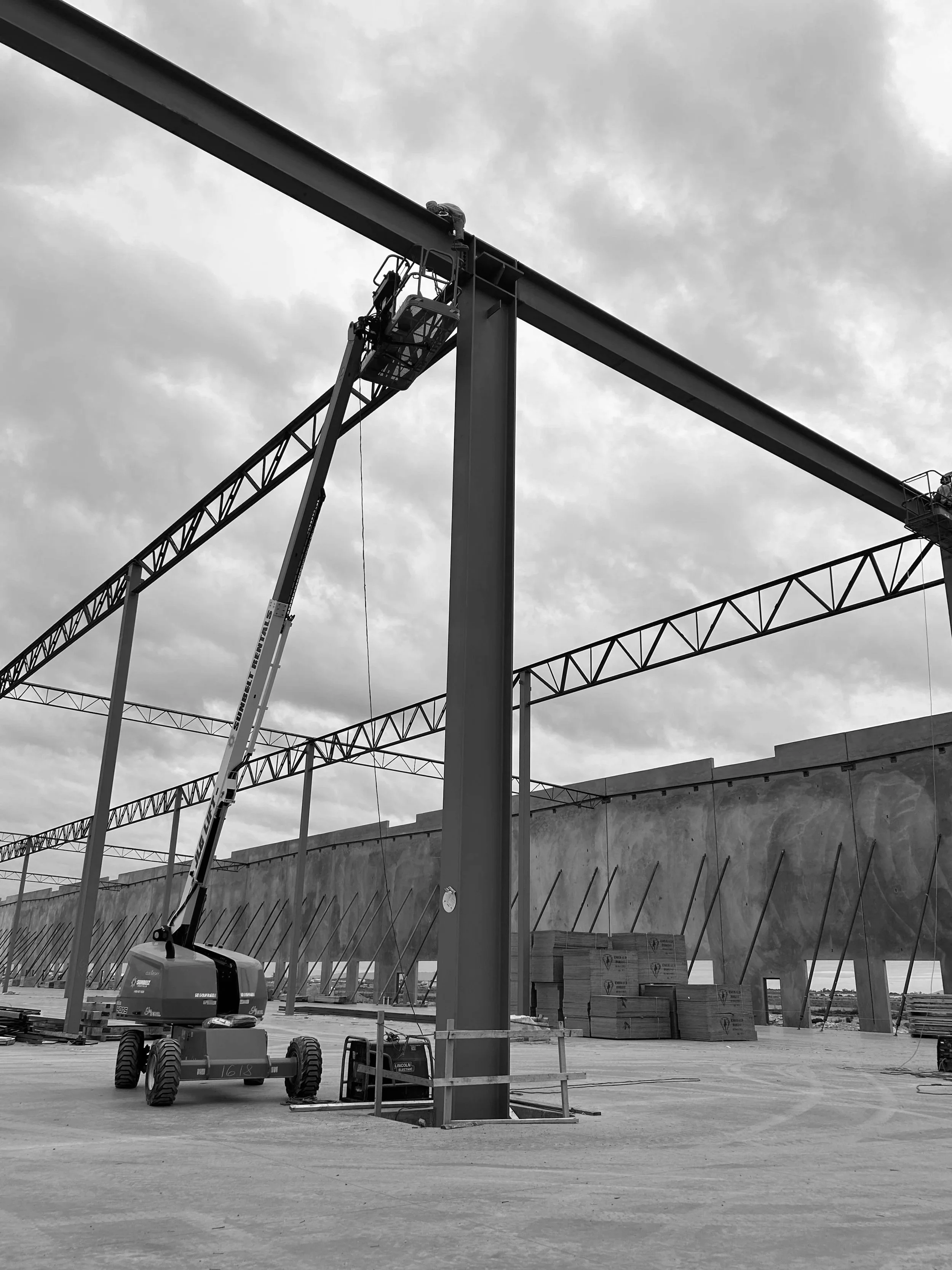 Construction site with steel beams, a construction lift, and large concrete walls. Overcast sky in the background.