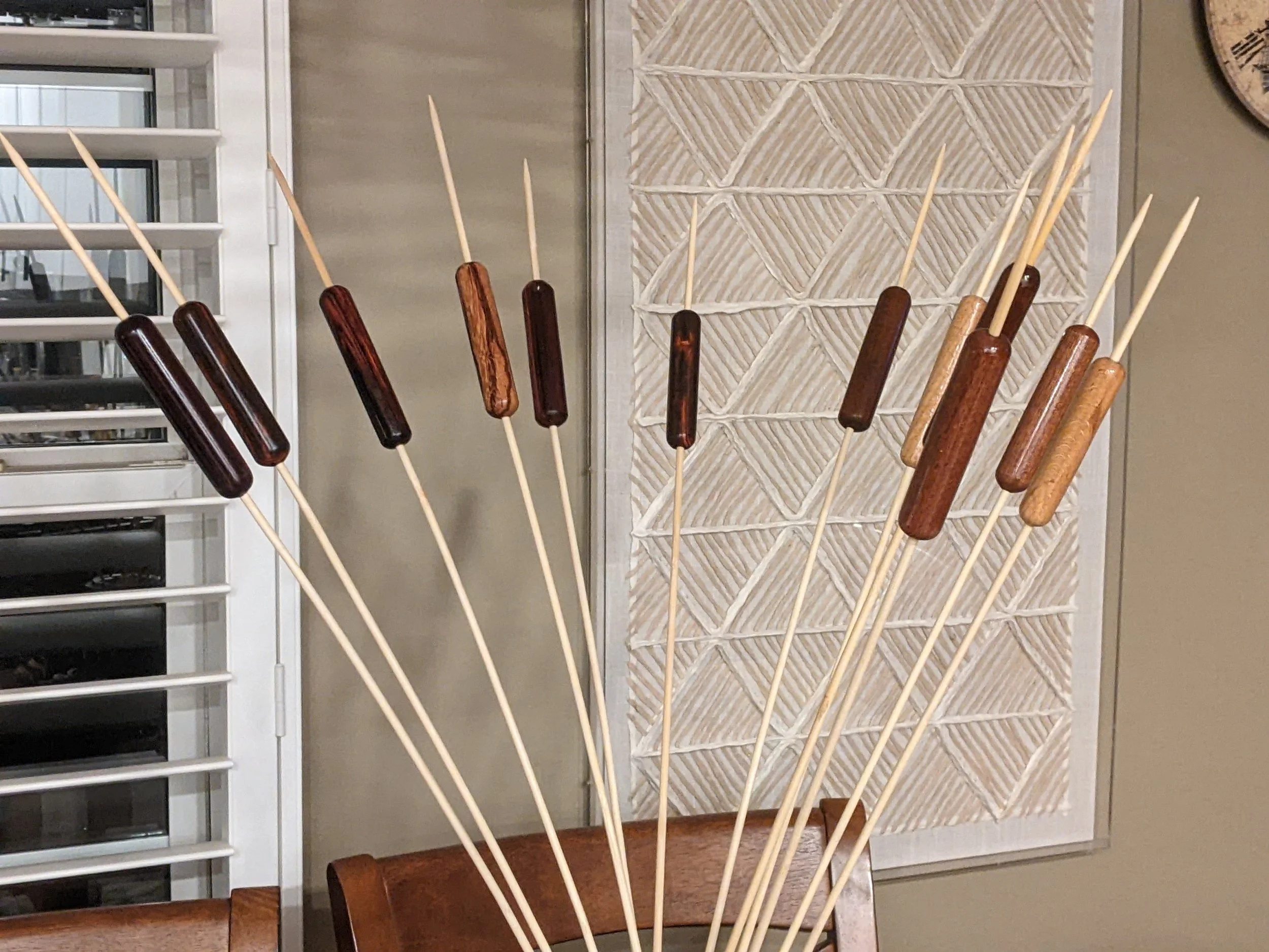 Cattails with dark and light wood pieces inserted, arranged in a fan shape on a dining chair.