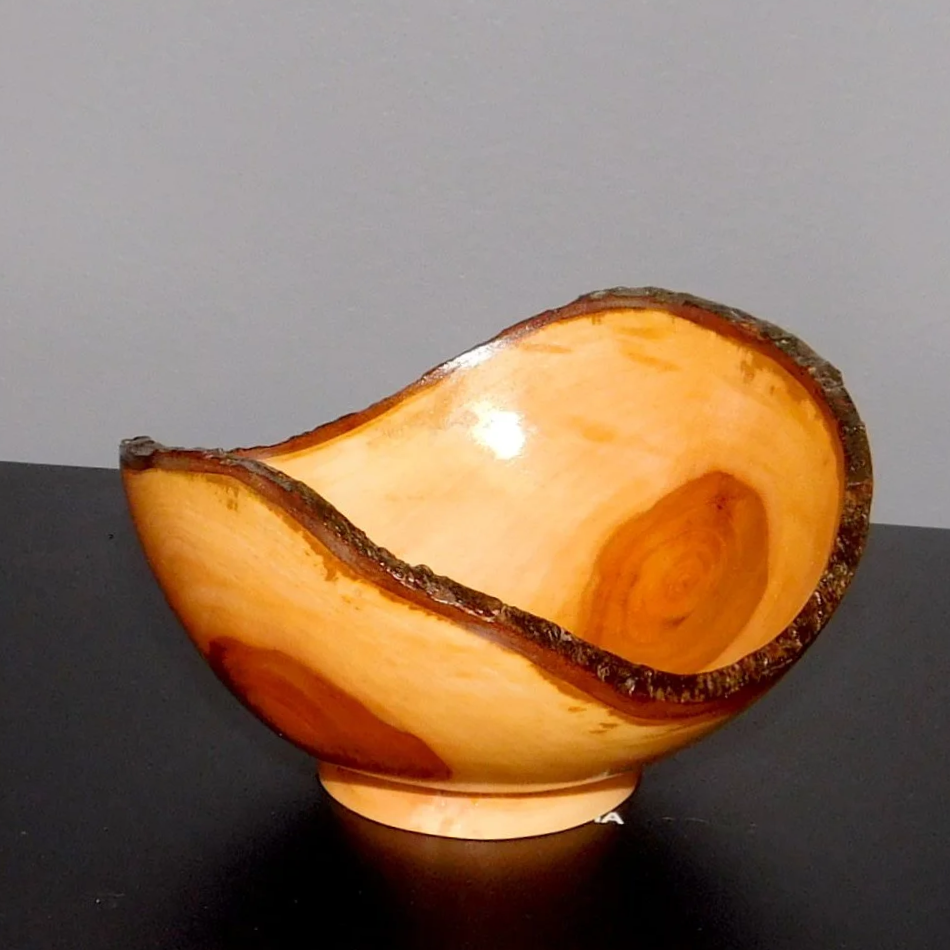 A decorative bowl made from a large, sliced piece of wood with bark edges and a polished interior, resting on a black surface.
