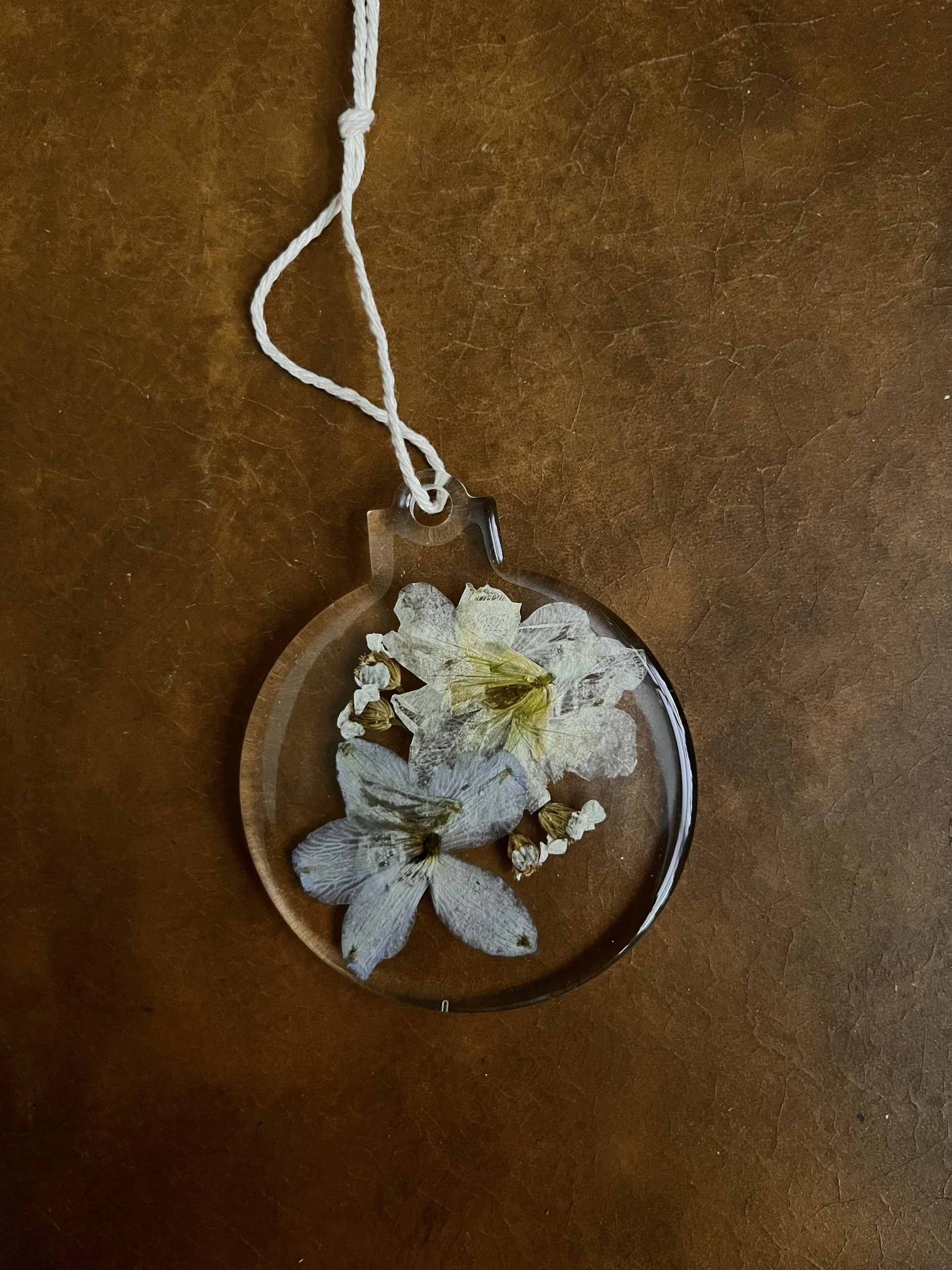 A clear pendant with dried flowers inside, attached to a white string, resting on a wooden surface.