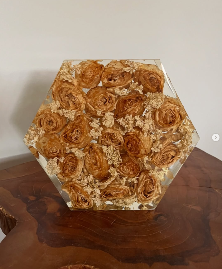 Decorative clear hexagonal vase filled with dried beige roses and floral elements, placed on a polished wooden surface.