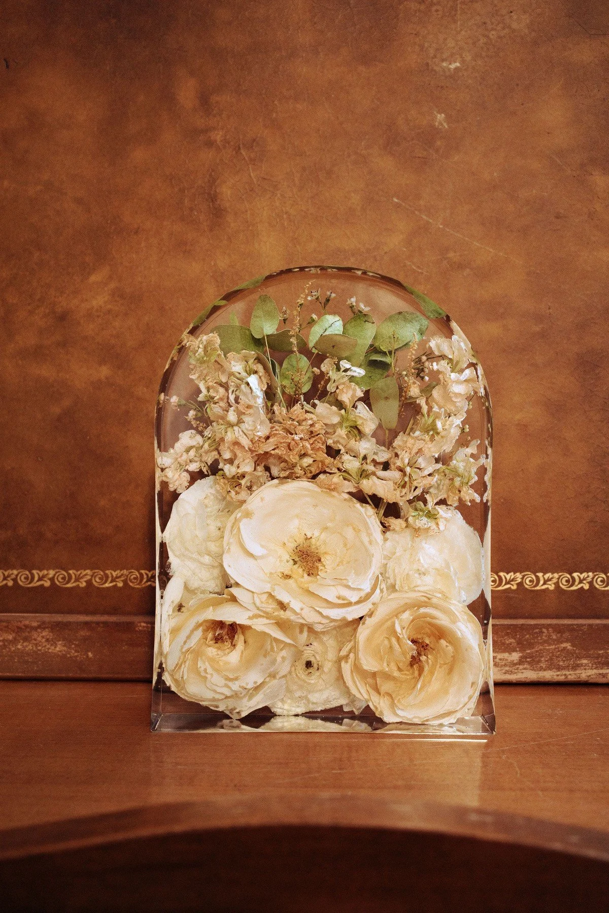 A glass container filled with white flowers and dried green leaves.