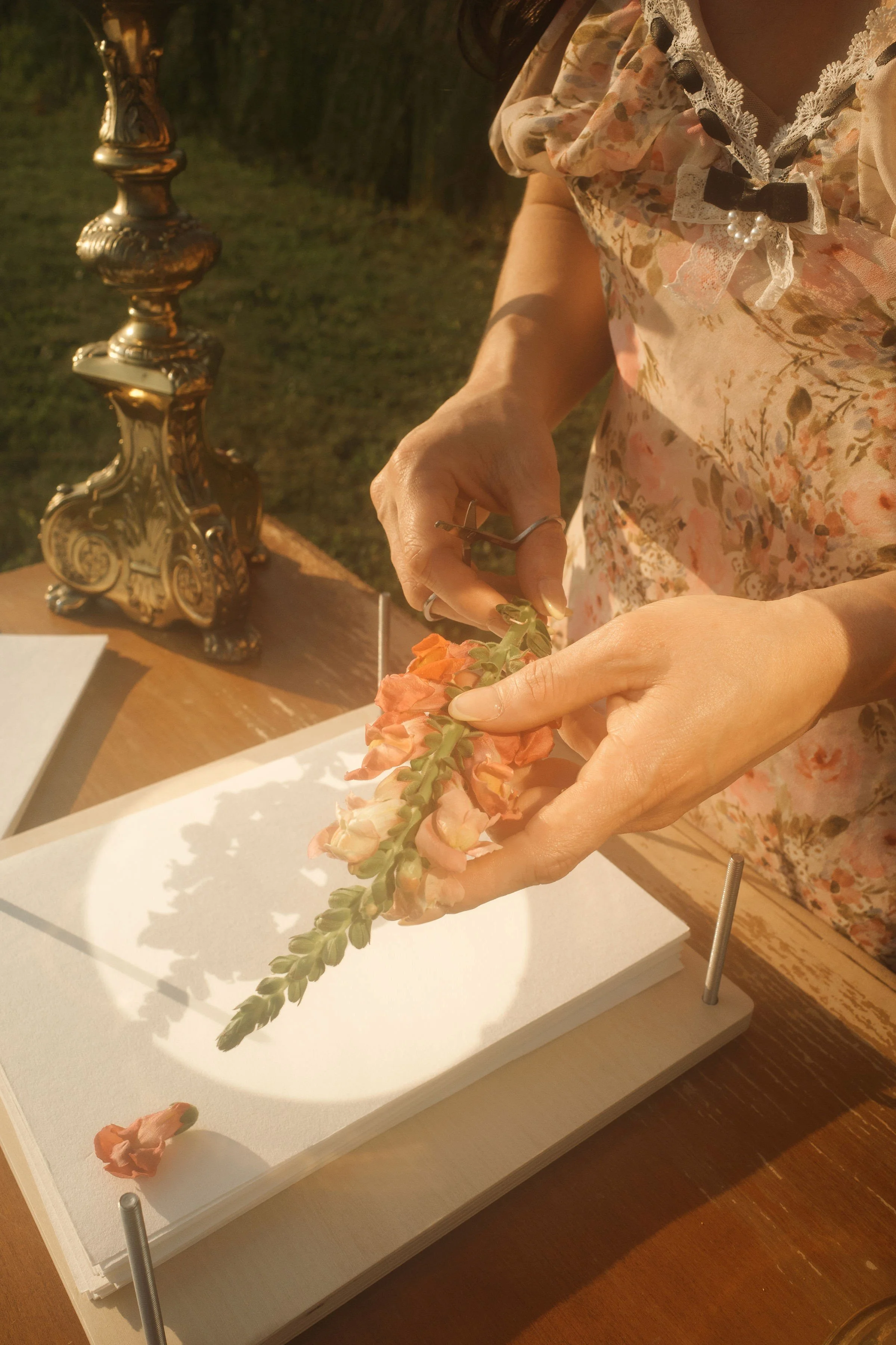 A person wearing a floral dress arranging flowers on a white canvas with a brass candlestick in the background.