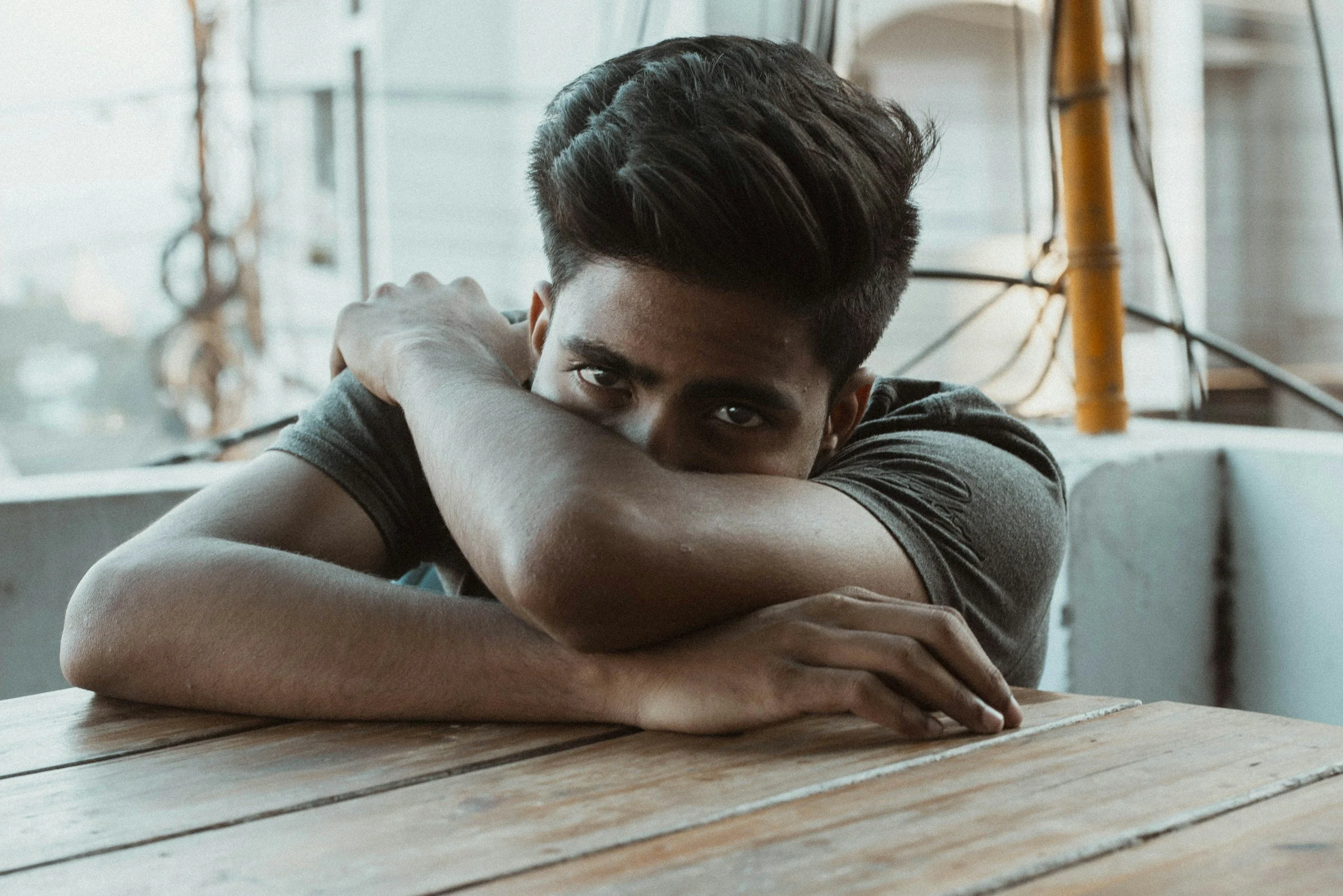Young man sitting alone at a table, appearing reflective and emotionally guarded.