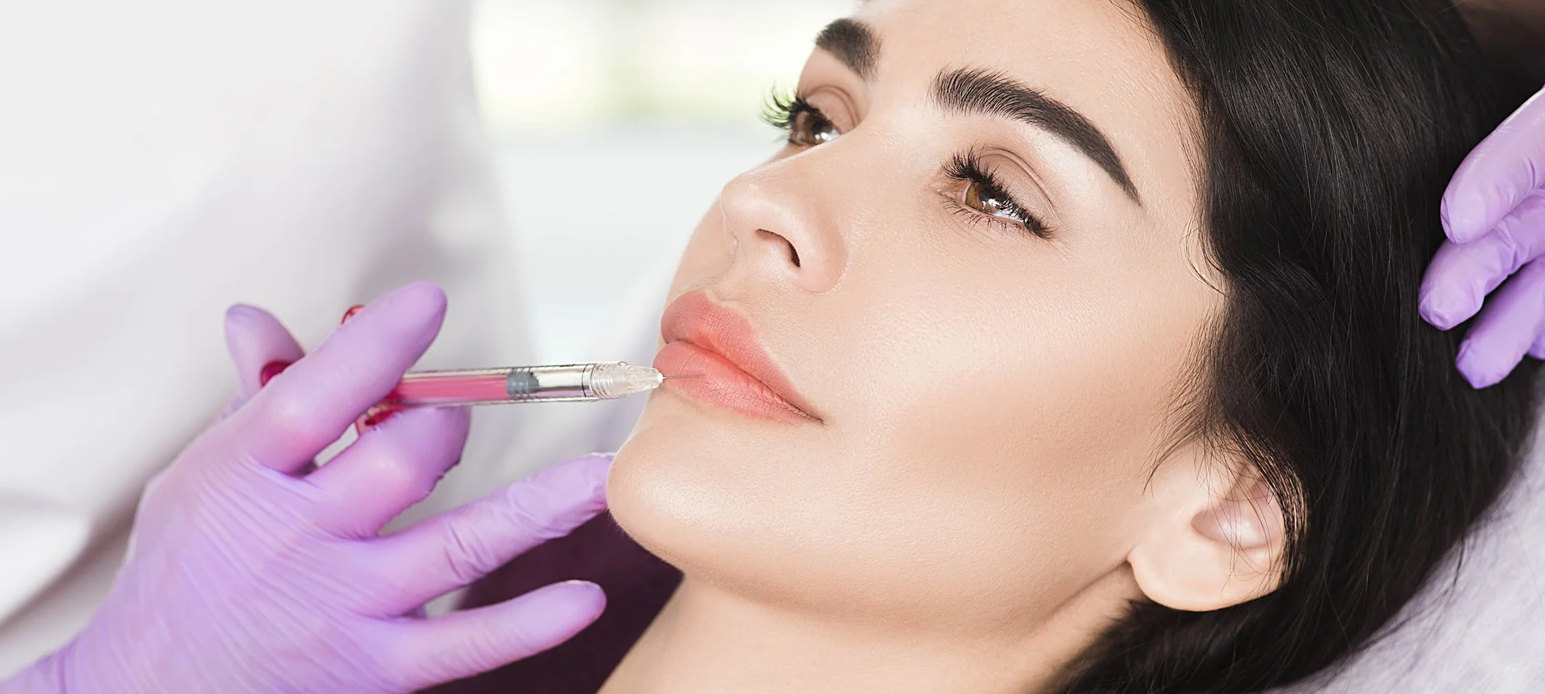 Woman receiving a cosmetic injection in her lips from a practitioner wearing purple gloves.