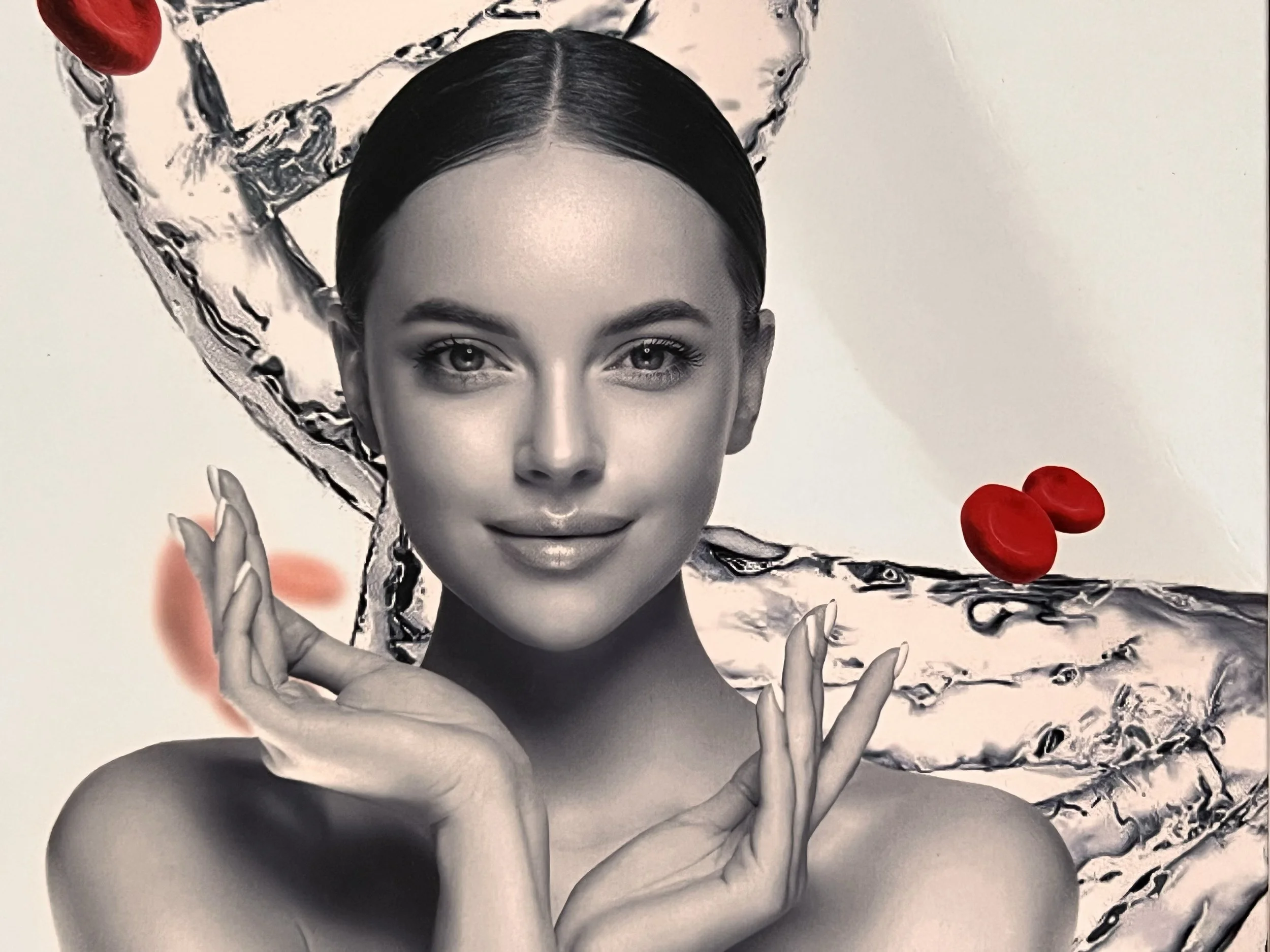 Black and white portrait of a woman with slicked-back hair, smiling subtly, with hands poised near her face. Background features a splash of water and a few red coffee beans.