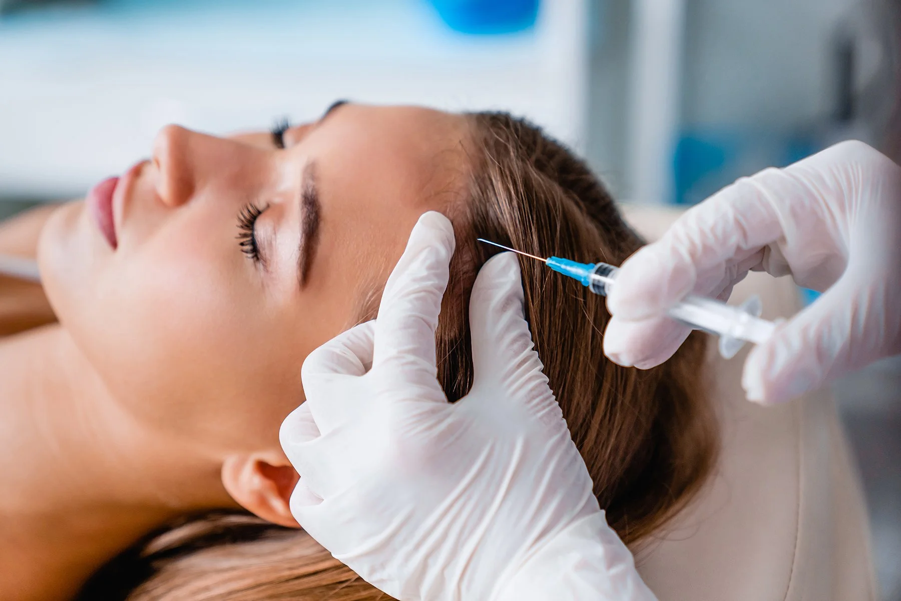 A woman is lying down during a cosmetic procedure, with a medical professional administering an injection into her forehead.