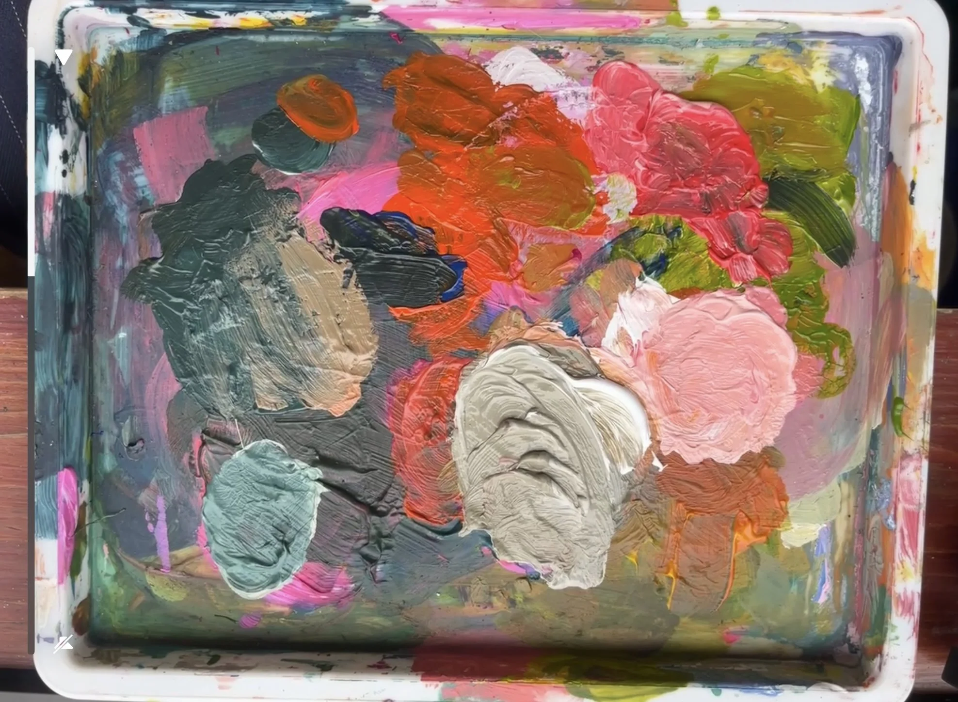A colorful abstract painting with thick brushstrokes in various colors including pink, red, green, black, gray, and white on a rectangular palette.