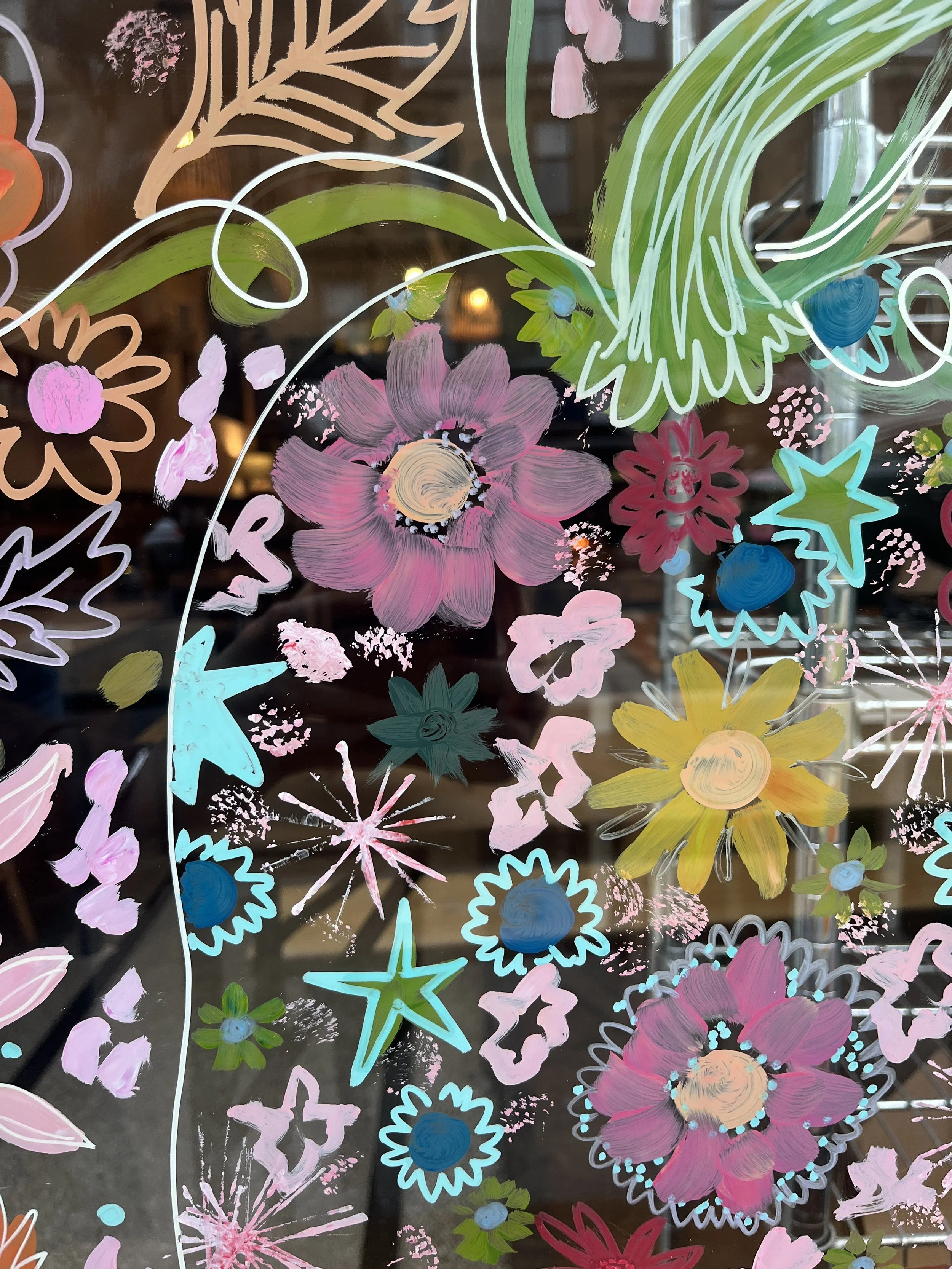 Colorful floral and star-shaped doodles painted on a glass surface.