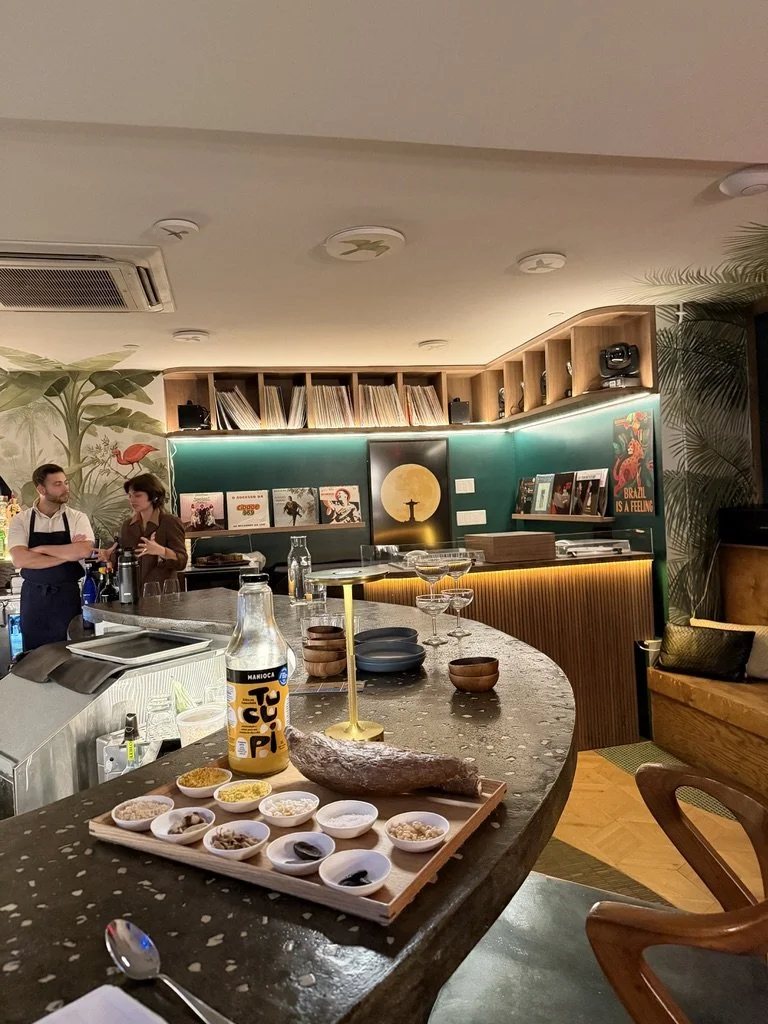 Chef Vitor and sommelier Hannah in conversation at a warmly lit bar counter inside a Brazilian restaurant