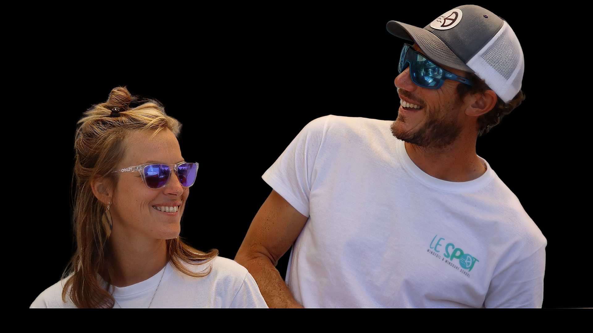 Un homme et une femme souriants portant des T-shirts blancs et des lunettes de soleil, le fond est noir.