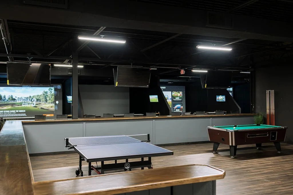 Indoor recreational space with a ping pong table, a pool table, and multiple screens mounted on the back wall.