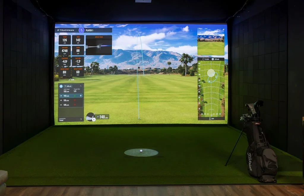 Indoor golf simulator displaying a scenic golf course with mountains in the background, various golf statistics, and a golf bag with clubs on the right side.