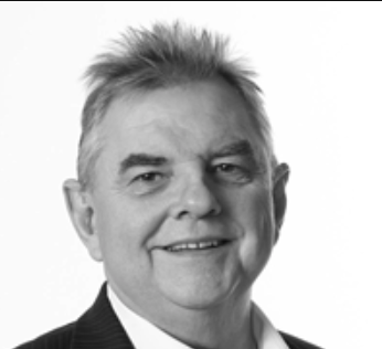 Black and white portrait of a smiling man with short, spiked hair wearing a suit.