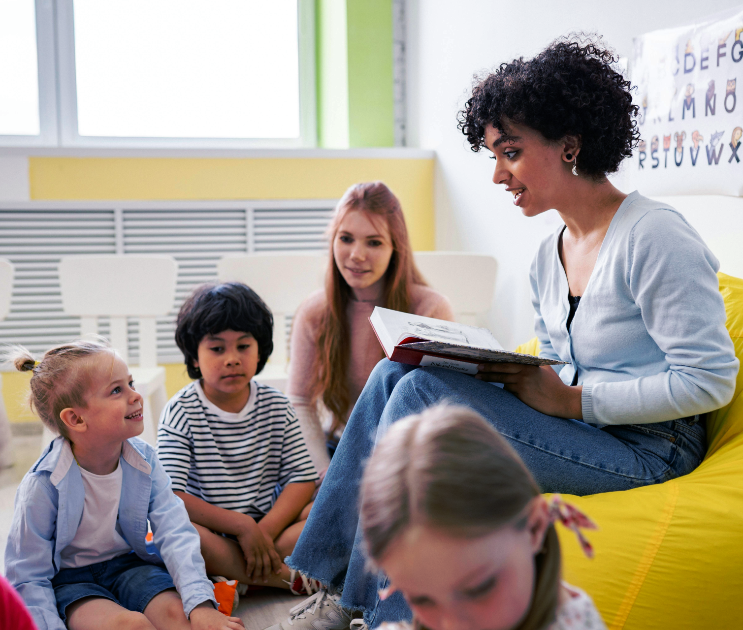 A teacher reading a storybook to a group of young children in a classroom.