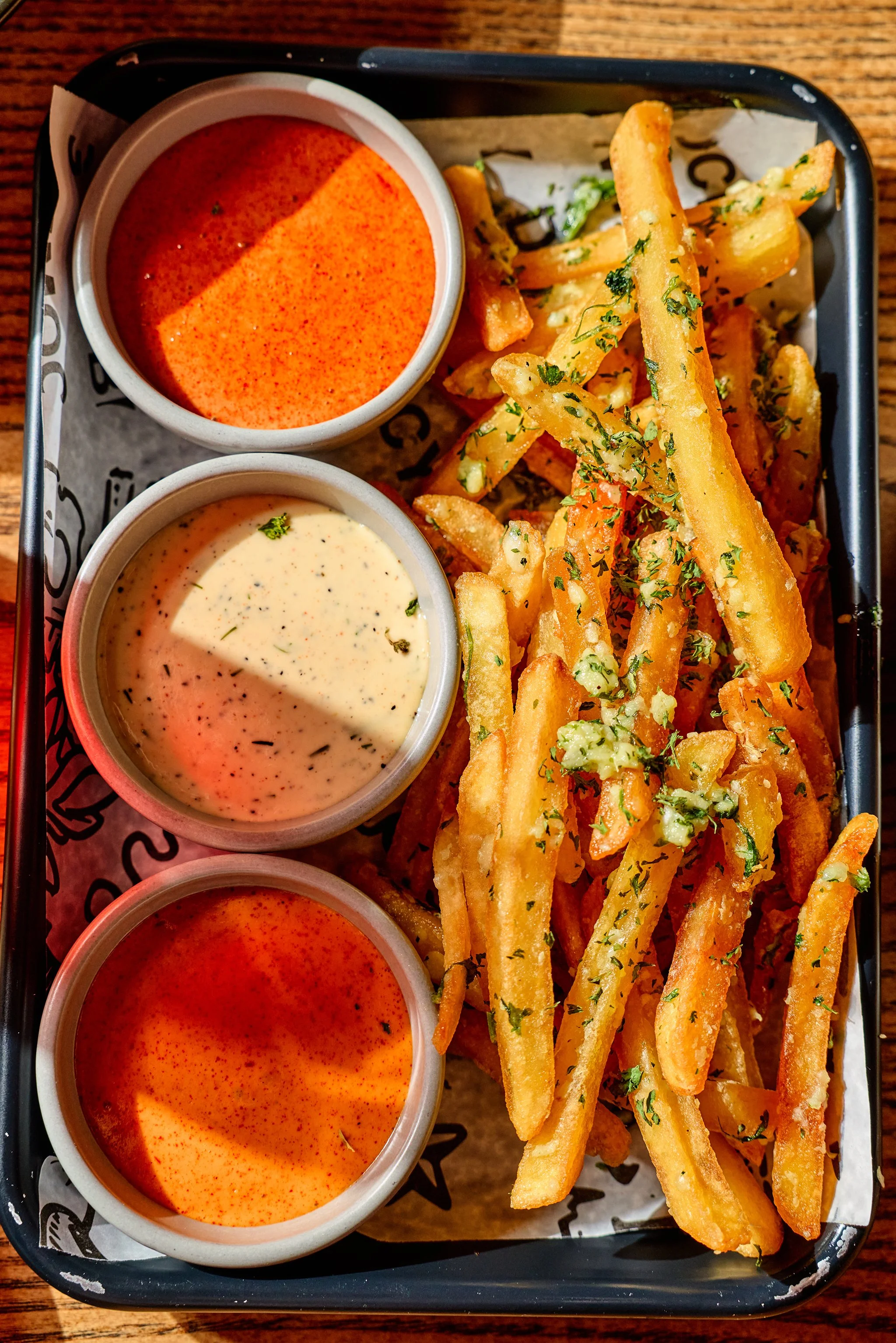 French fries garnished with chopped herbs served with three dipping sauces in small cups.