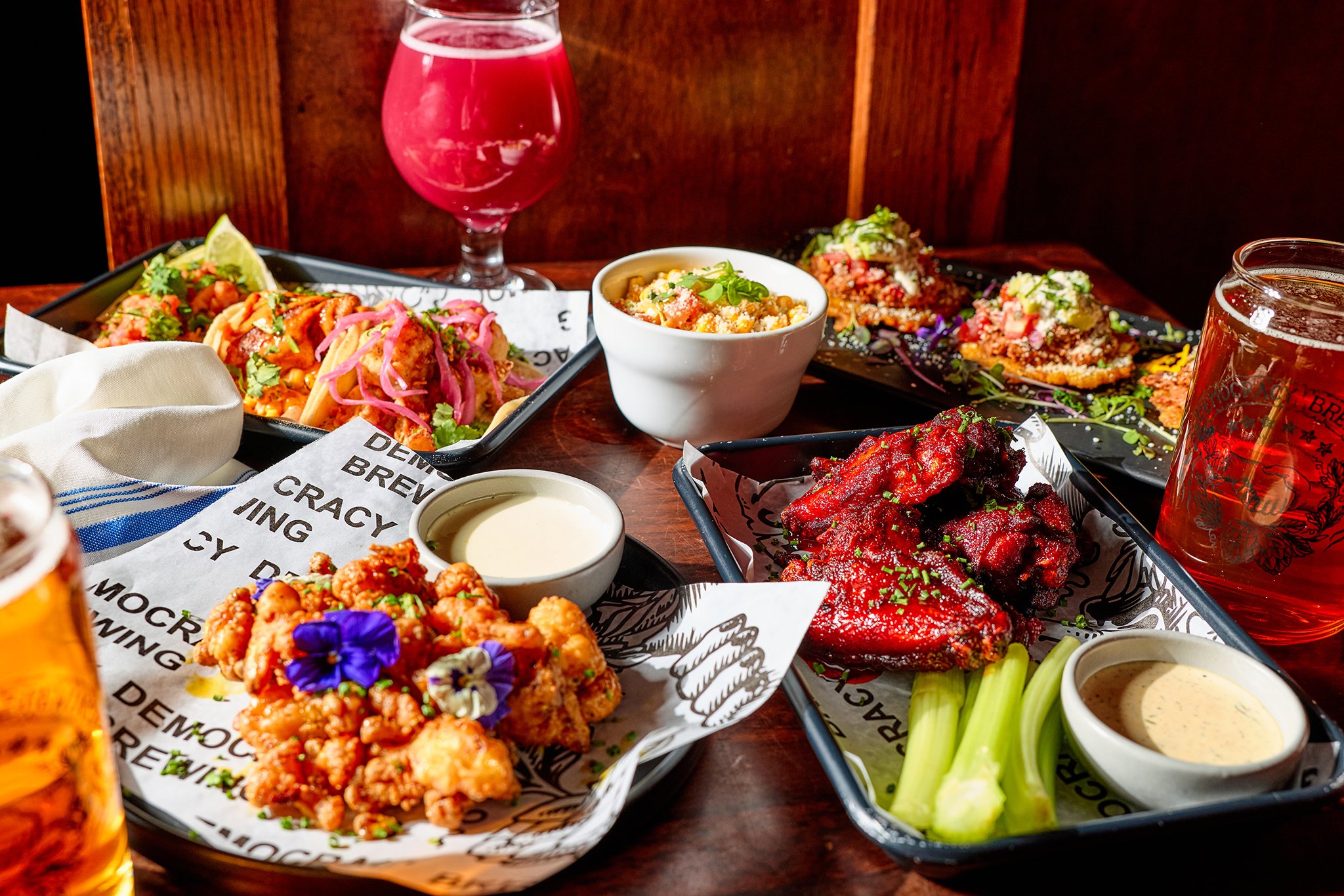 Assorted plates of Asian cuisine including fried chicken, spicy ribs, and tacos, with drinks on a wooden table.