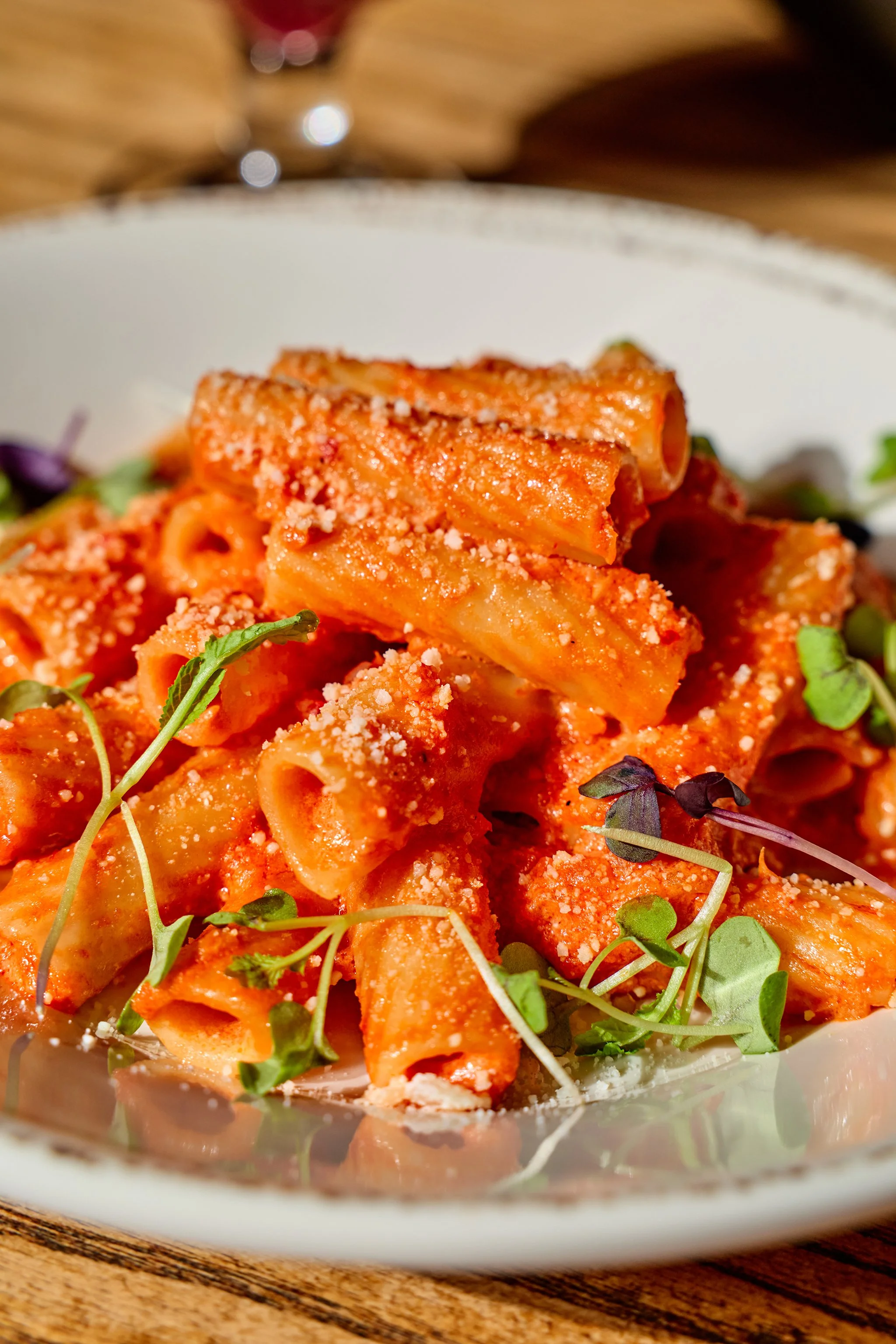 Plate of pasta with tomato sauce, grated cheese, and garnished with microgreens, on a wooden table.