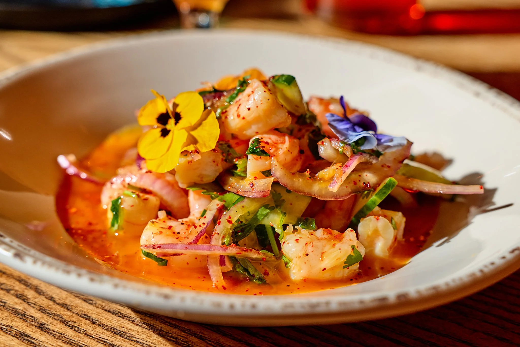 A plate of seafood salad with shrimps, octopus, and vegetables, garnished with edible flowers, on a wooden table.