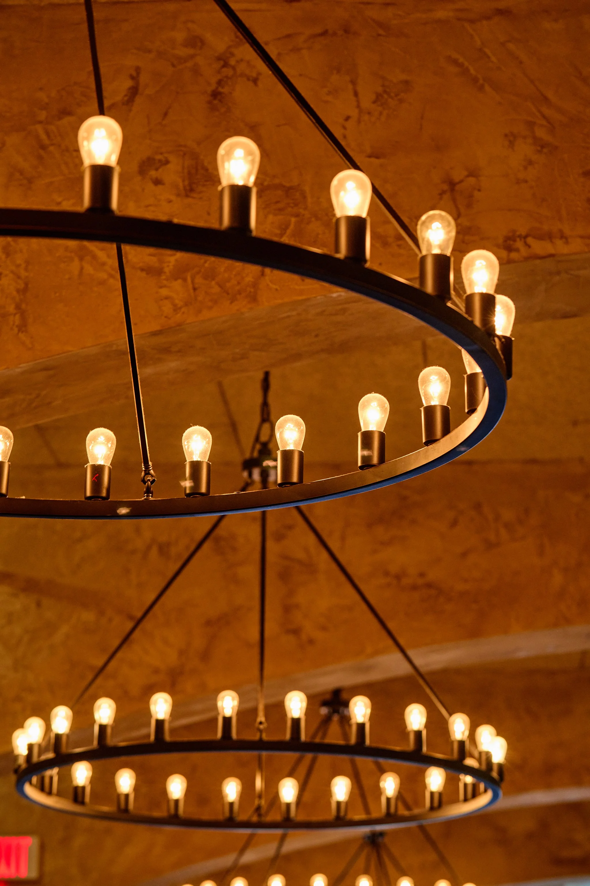 Two circular chandelier light fixtures with multiple exposed light bulbs hanging from a ceiling.