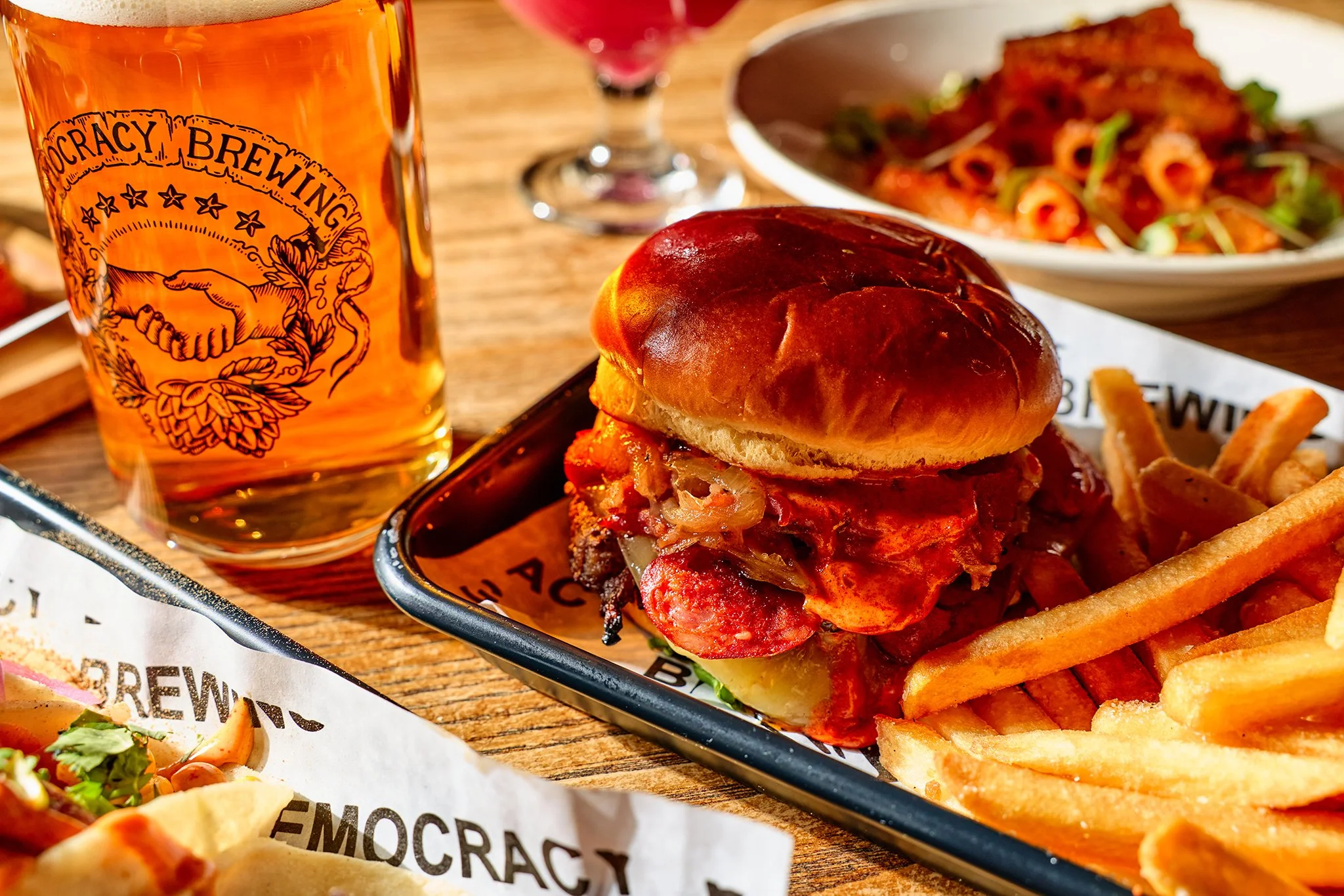 A cheeseburger with French fries, a glass of beer, and a bowl of pasta on a restaurant table.