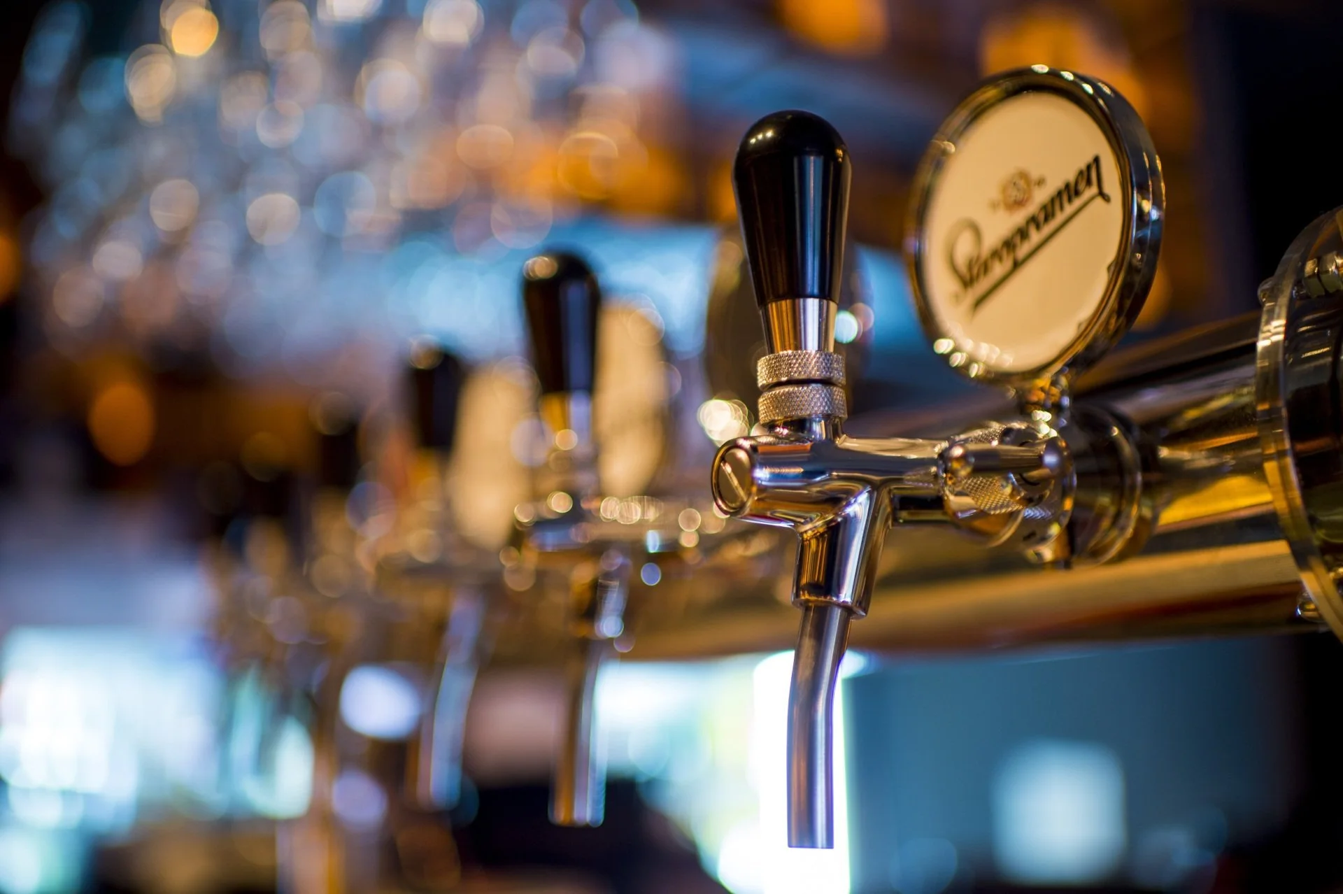 Close-up of beer tap handles on a bar counter, with a focus on the tap handle with the 'Perrier' logo, and blurred background.