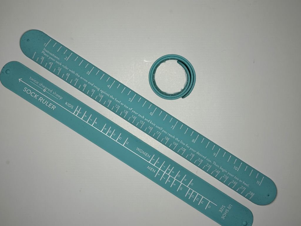 Sock ruler stretched out with one side of shoe sizes marked, one side with a metric and inch ruler, and the ruler rolled up