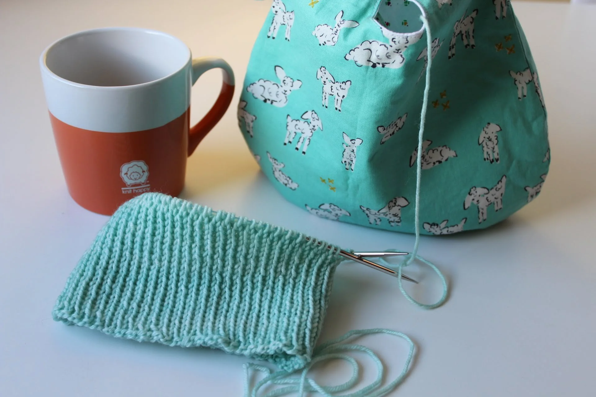 Blue sofa with a dark blue tote bag containing yarn and a knitting needle on it.