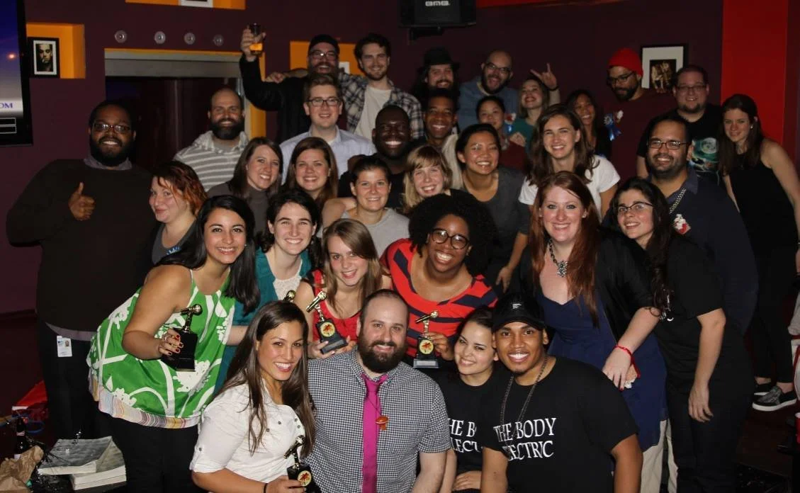 A large group of people posing together indoors, some holding awards, celebrating a special event or achievement.
