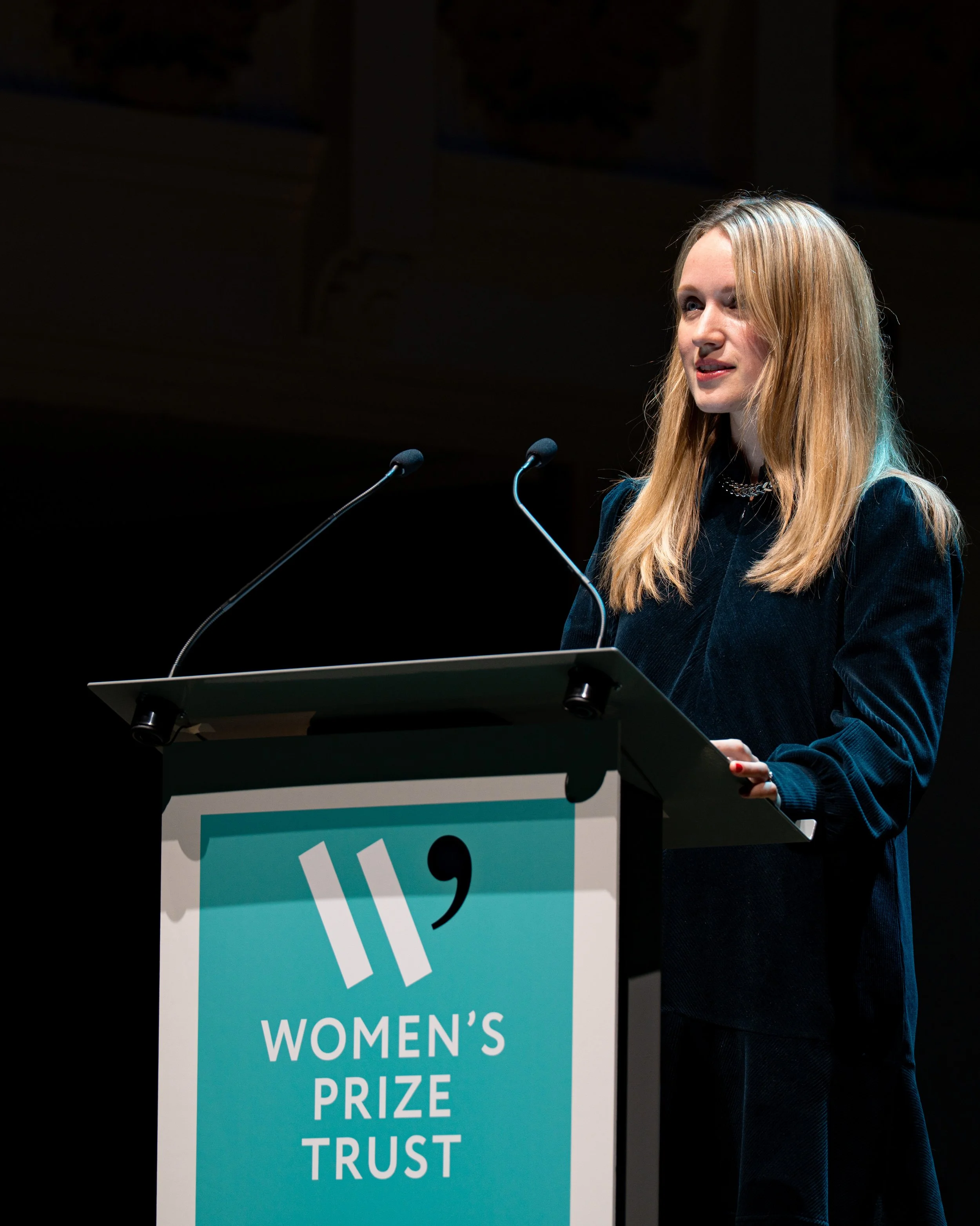 A woman with long blonde hair gives a speech at a podium during the Women's Prize Trust event.