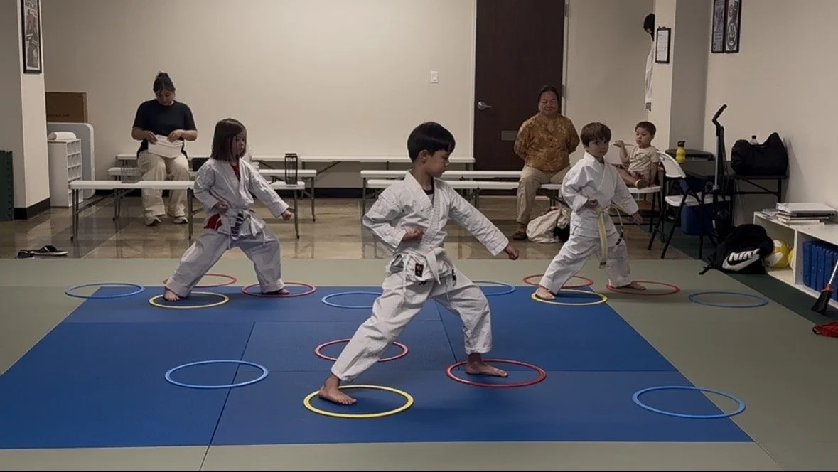 Children practicing martial arts in a dojo with colorful exercise hoops on the floor.