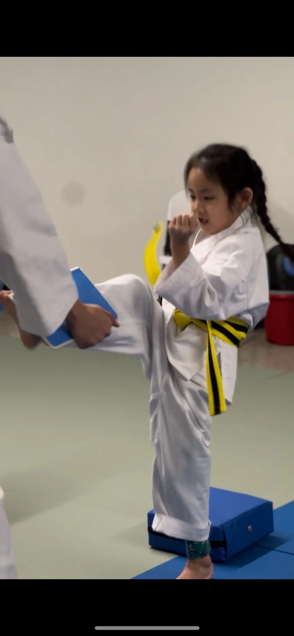 Young girl in a karate uniform with a yellow belt practicing a martial arts kick in a dojo.