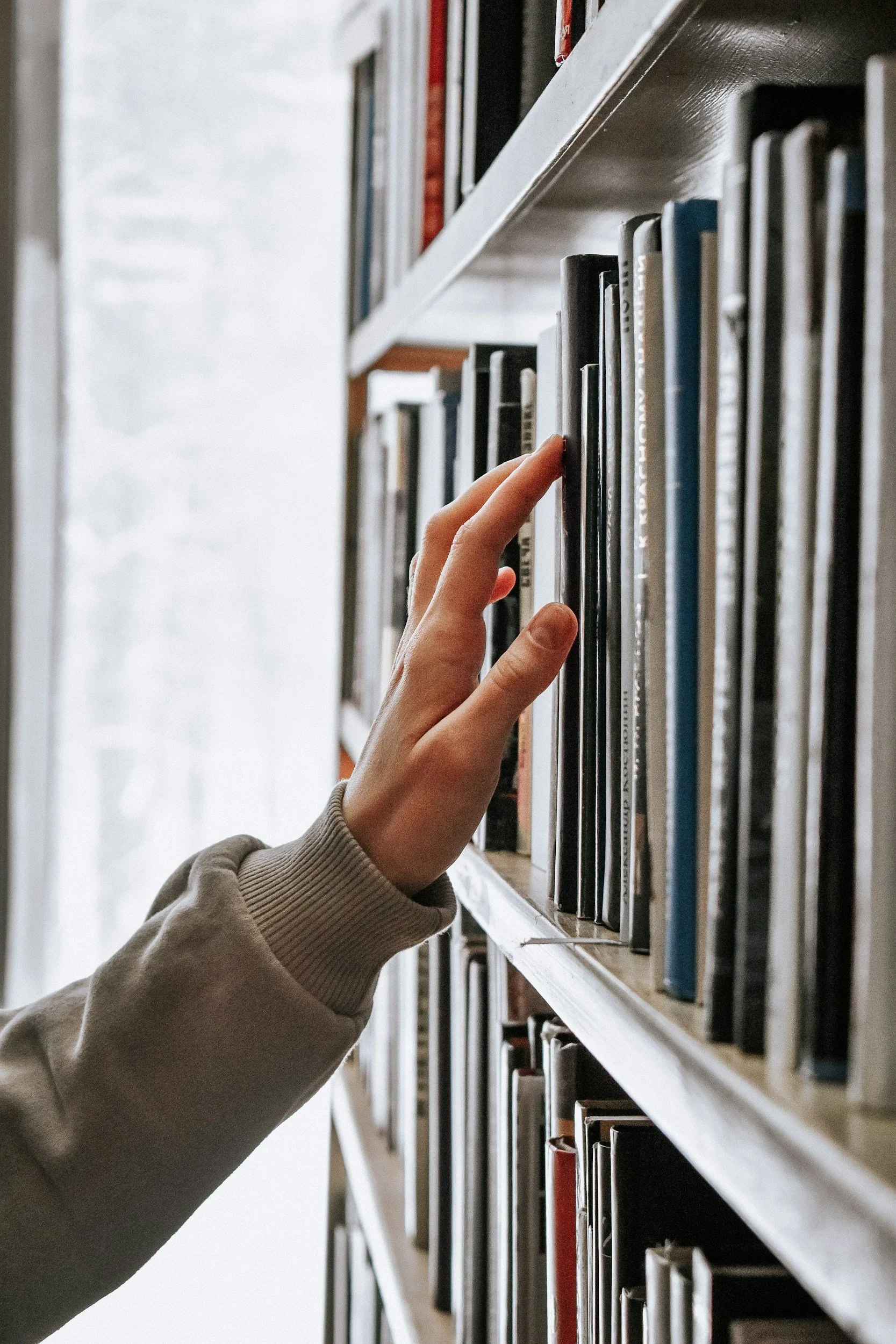 A person's hand reaching for a book on a bookshelf filled with books.