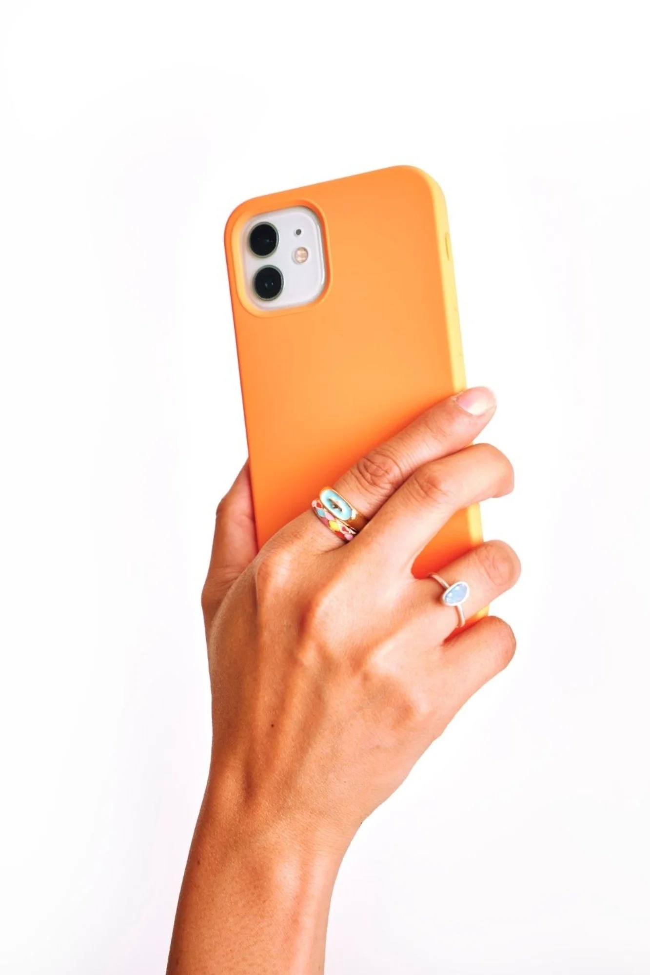 Person holding a smartphone with an orange case against a white background, wearing colorful rings.