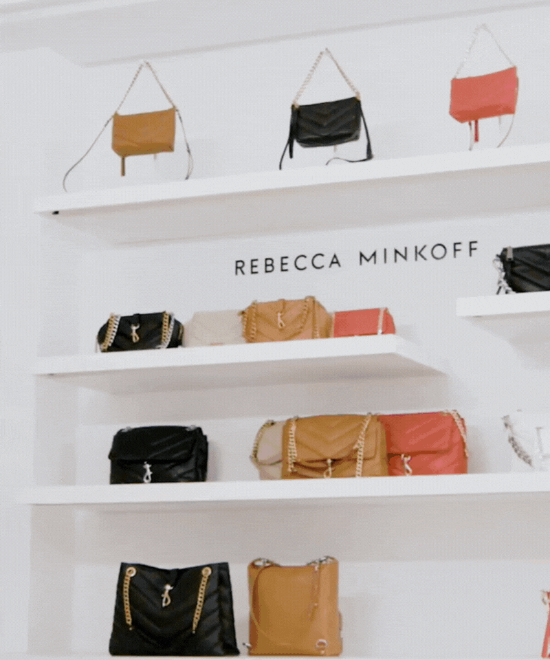 Display of designer handbags on white shelves with Rebecca Minkoff logo in the background.