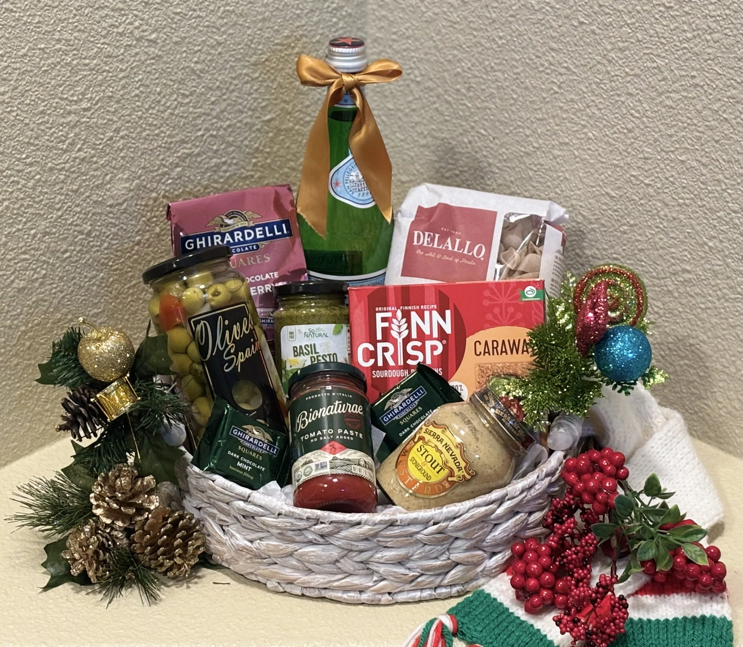 Holiday gift basket filled with food items, decorated with Christmas ornaments, pinecones, and holly berries.